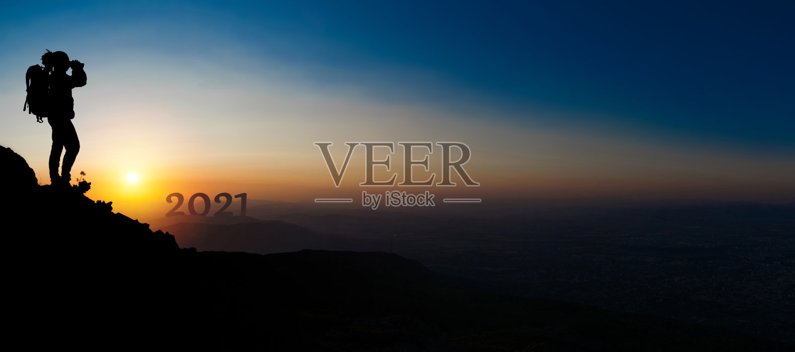 一个人爬上山顶，用双筒望远镜望着新年照片摄影图片