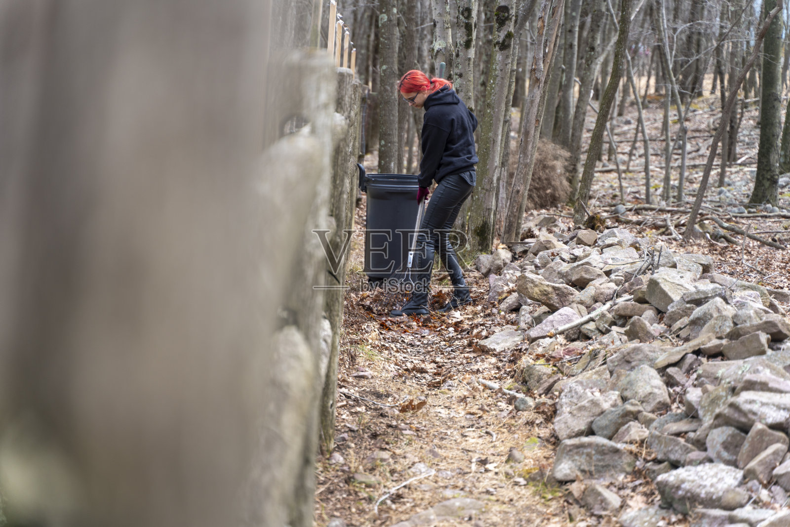 晚秋时节，红发少女在清理后院的老树叶。用树叶装满垃圾桶。照片摄影图片