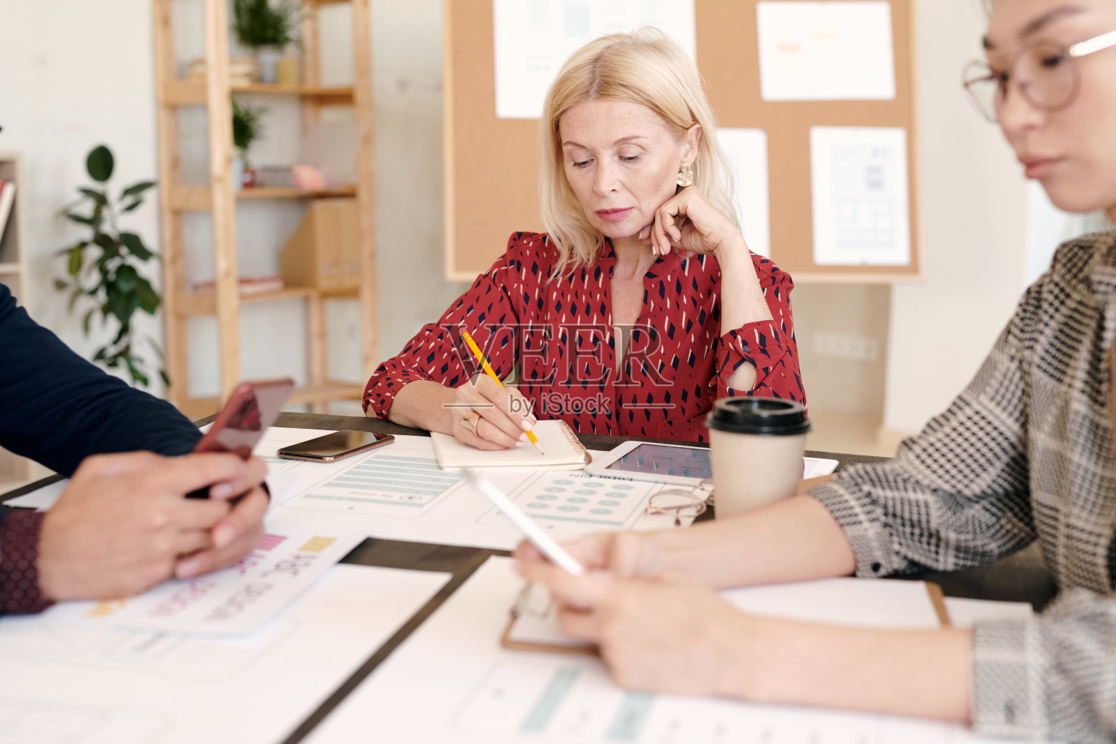 成熟的金发女性手机应用程序开发人员在笔记本上做笔记照片摄影图片