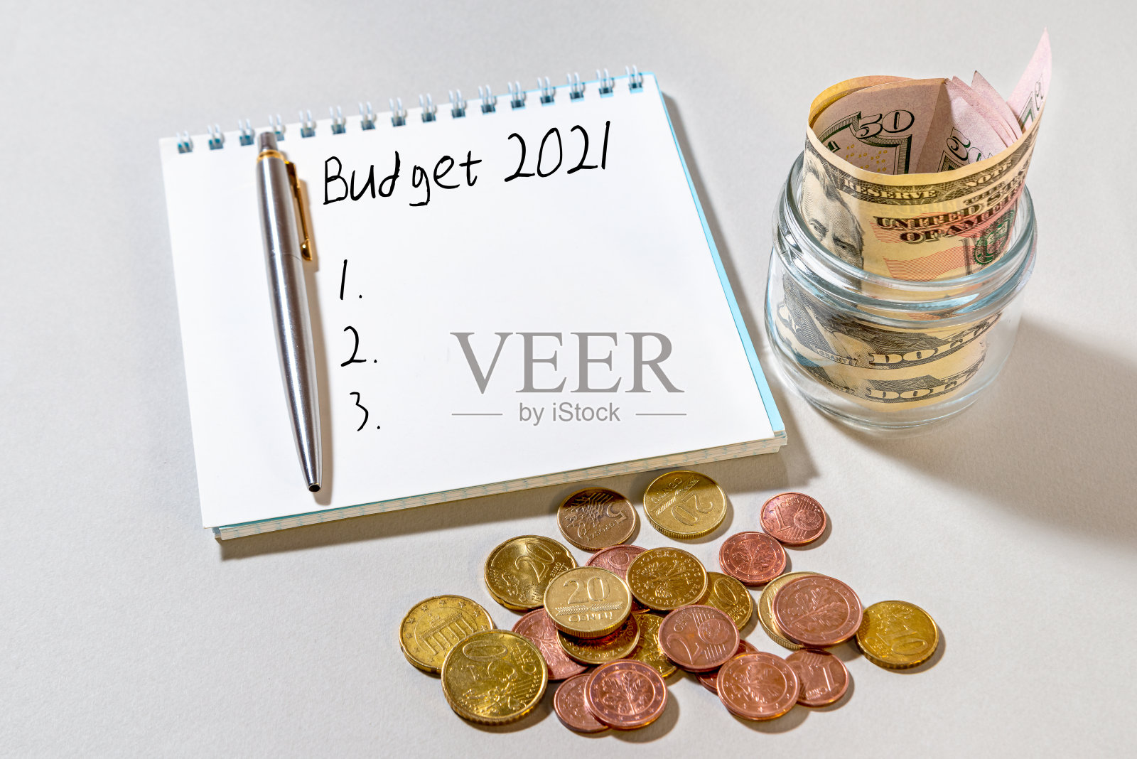 一个装着美元的玻璃罐，散落的硬币和一个写着“2021年预算”的笔记本。-经济的概念。照片摄影图片