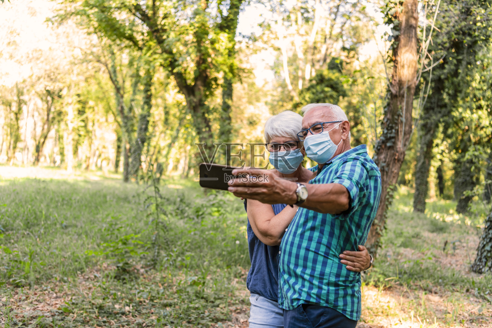 一对老年夫妇自拍或视频与家人通话，庆祝解除冠状病毒封锁。退休男女在公园里用智能手机自拍，享受退休生活。照片摄影图片