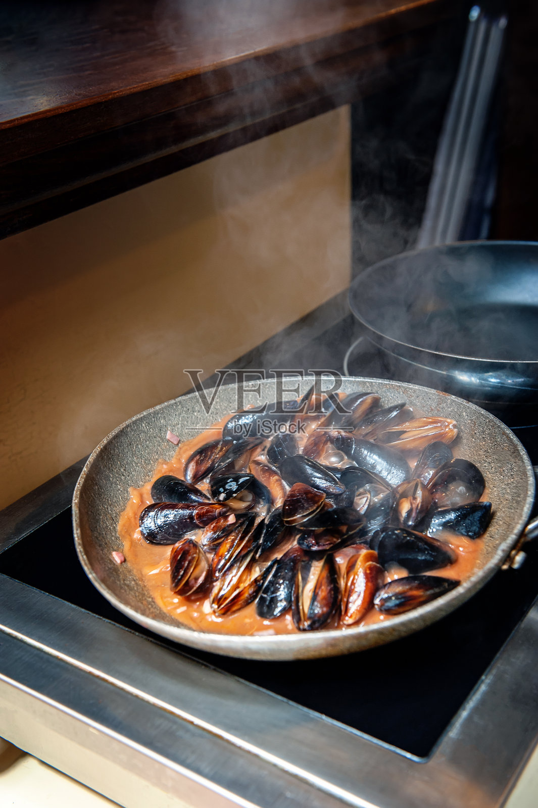新鲜的贻贝用美味的奶油酒酱在平底锅里煮熟。在餐馆里烹饪贻贝的特写。有选择性的重点照片摄影图片