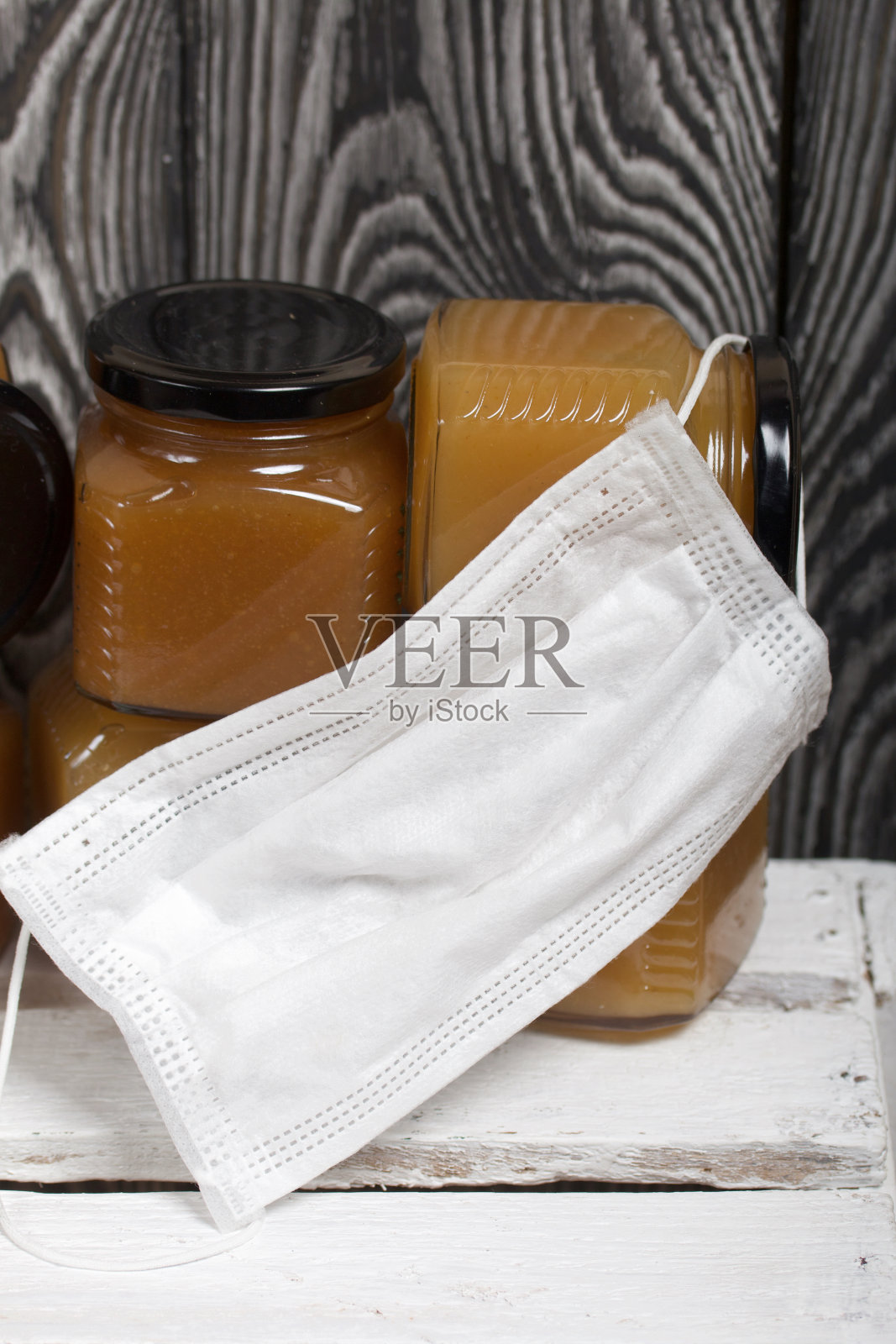 罐装果酱。他戴着医用口罩。站在一个白色的木箱上。以黑色松木板为背景。照片摄影图片