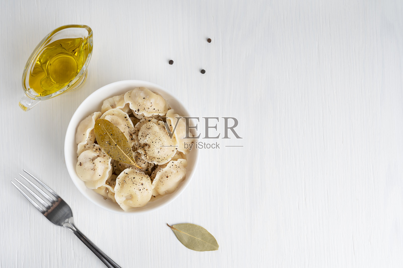 平铺着俄罗斯自制的帕尔梅尼食物，碗里放着叉和油，放在白色的木桌上照片摄影图片