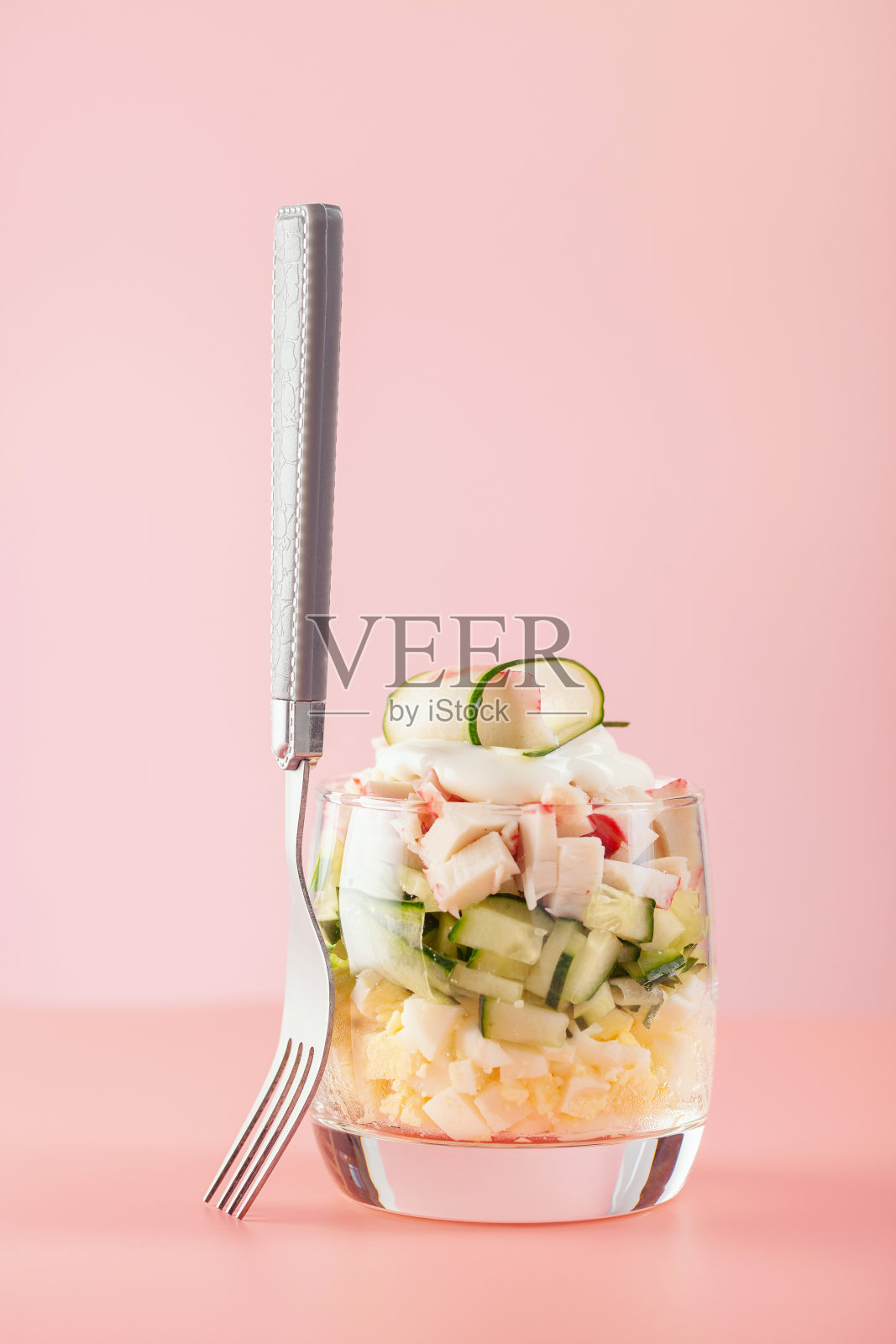 蟹肉棒，黄瓜，鸡蛋和玉米的沙拉，在粉红色的背景上。俄罗斯的节日食品照片摄影图片