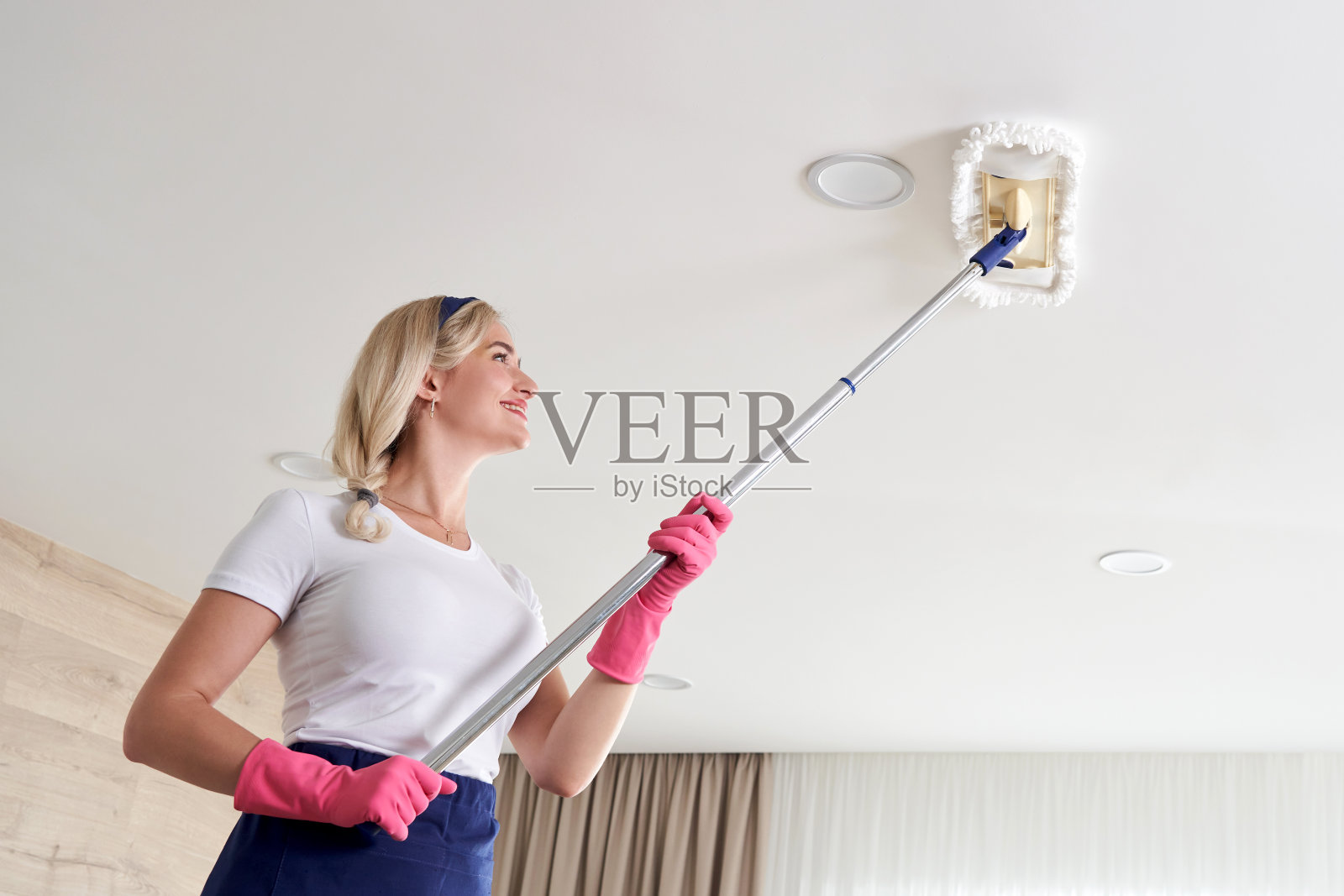 女佣拿着拖把堆，打扫客厅天花板。房屋清洁服务理念照片摄影图片