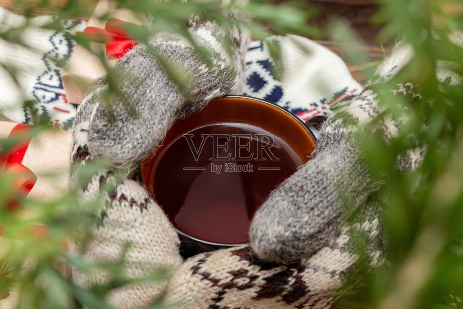 手在连指手套举着茶杯茶近距离上的棕色毛刷木松树枝礼物玩具的背景。秋叶hygge, fika, lagom，舒适，温暖，放松的假期概念照片摄影图片