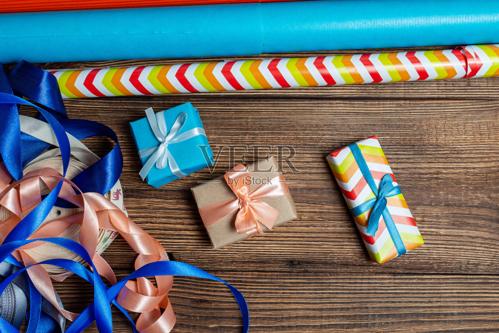 礼品盒和彩色包装纸与丝带在木制的棕色背景。为新年和圣诞节做准备的概念。照片摄影图片