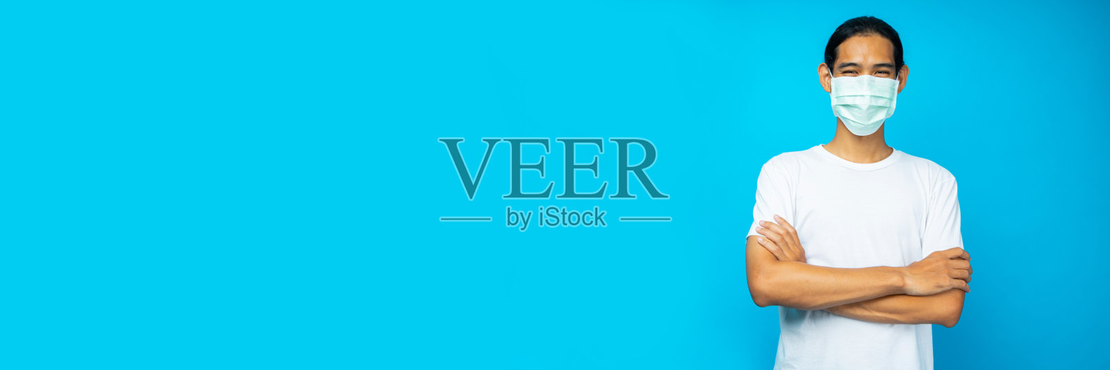 亚洲男子的肖像戴着面具双臂交叉，微笑孤立在蓝色背景照片摄影图片