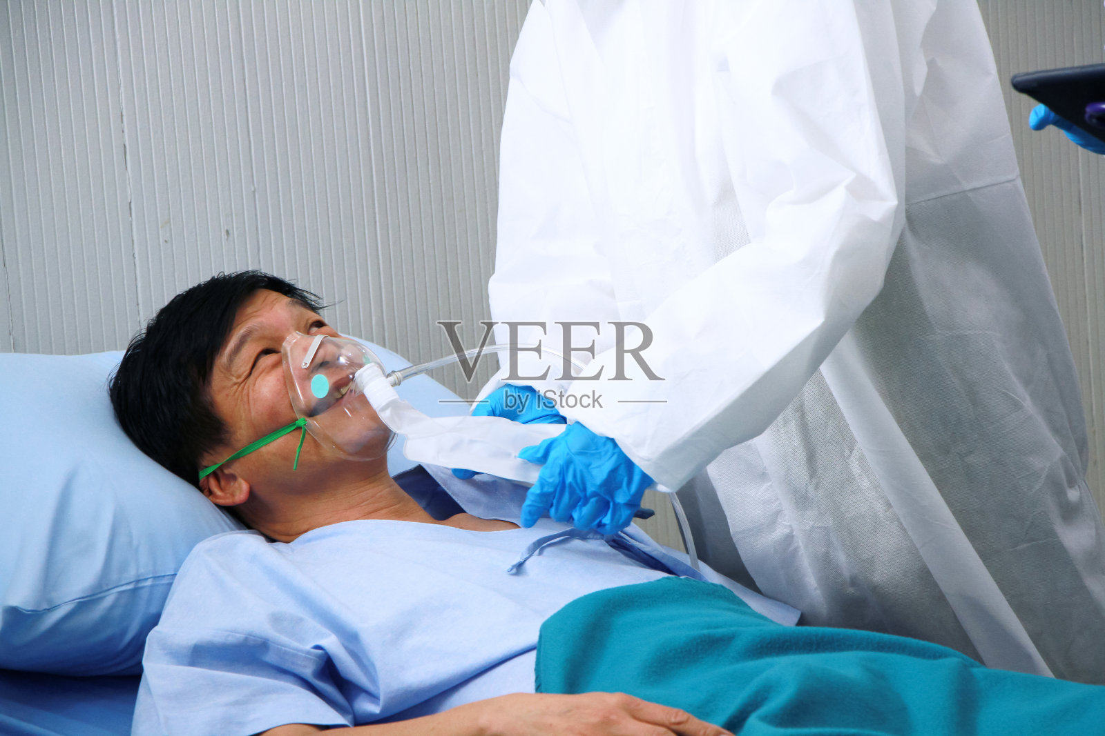 医疗团队在个人防护装备或个人防护服和使用呼吸器的亚洲老年患者是呼吸系统感染Covid - 19病毒，研究用片剂治疗。照片摄影图片