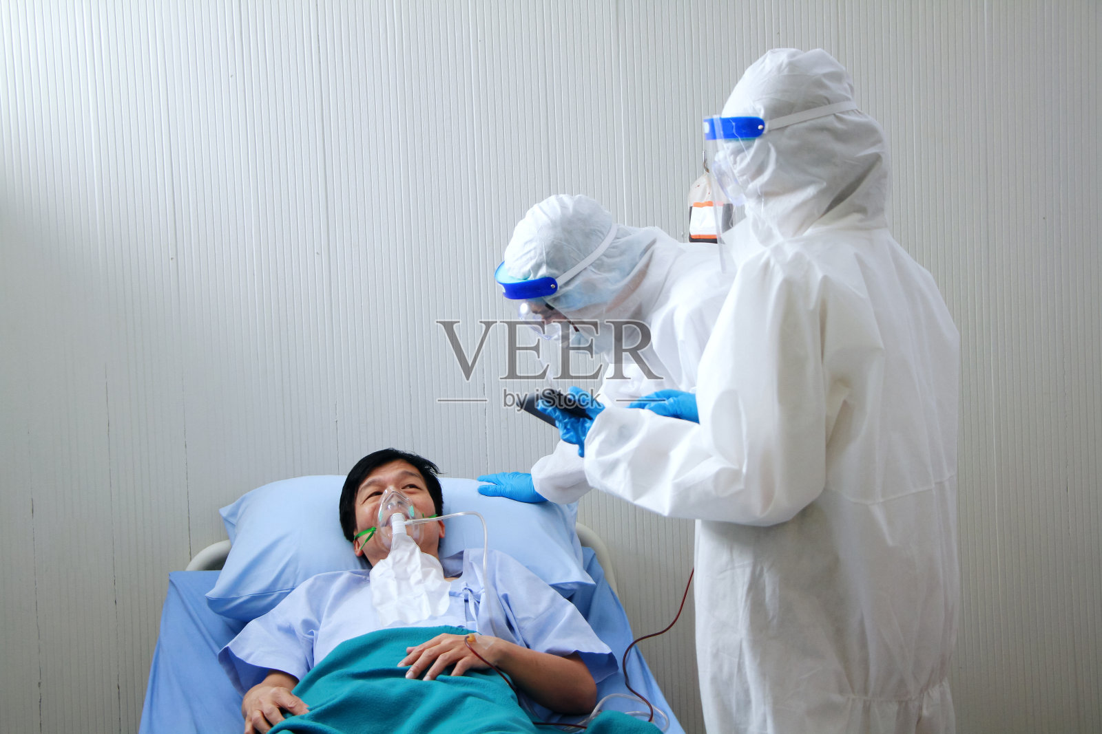 医疗团队在个人防护装备或个人防护服和使用呼吸器的亚洲老年患者是呼吸系统感染Covid - 19病毒，研究用片剂治疗。照片摄影图片