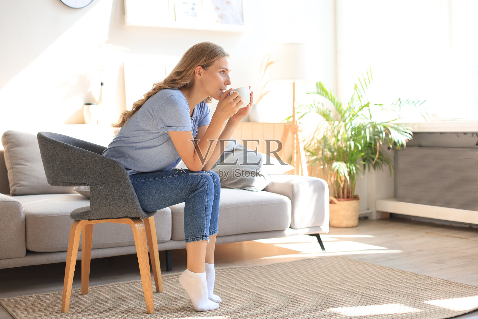 坐在扶手椅上喝咖啡的年轻女子。照片摄影图片