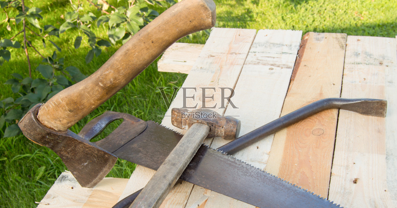 建筑工具锤子，斧头，钢锯架，躺在花园里的灯板上照片摄影图片