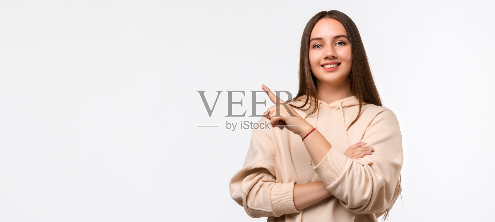 快乐漂亮的年轻女子与长栗色头发，指着手指的一边，显示复制空间为您的信息照片摄影图片