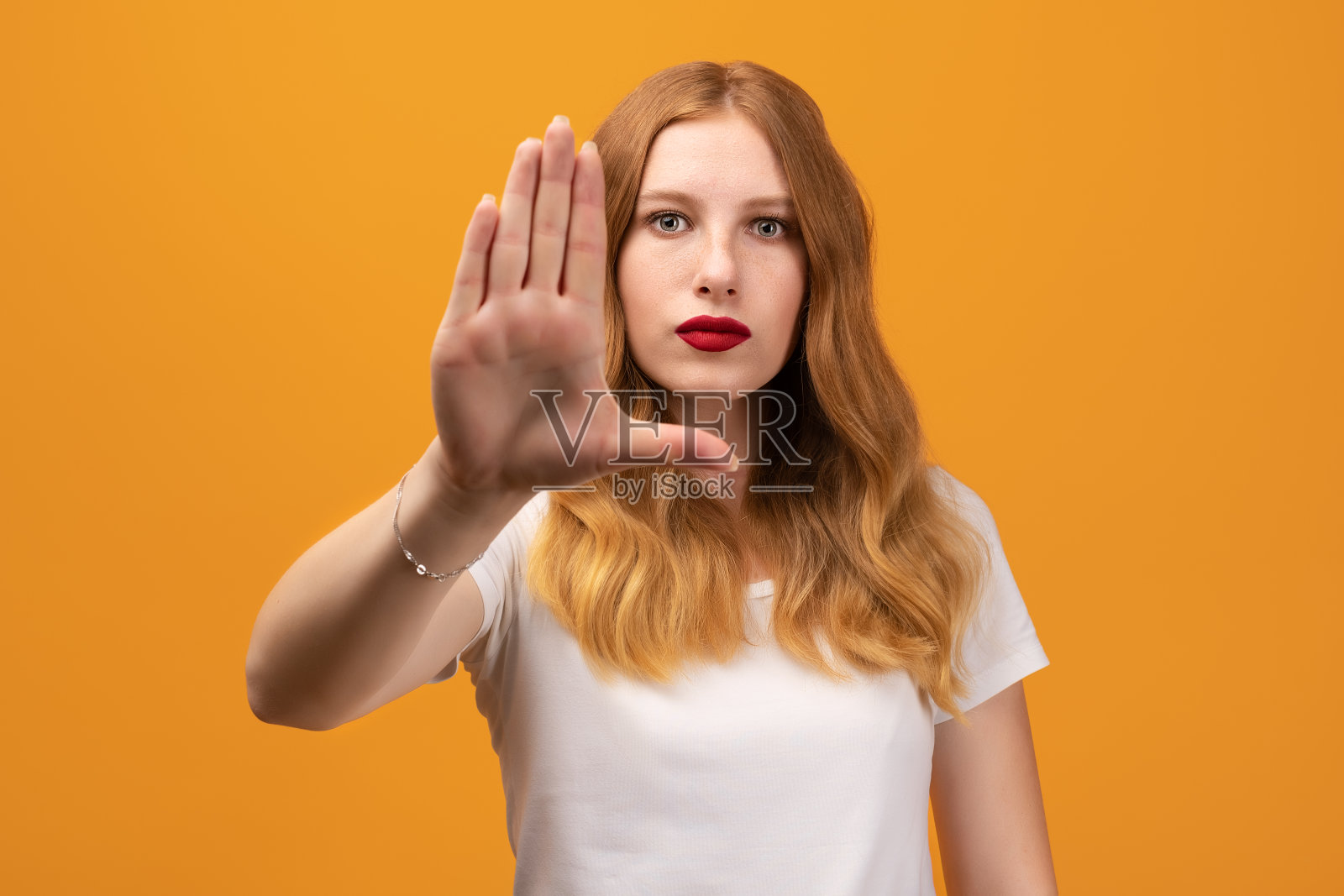 年轻漂亮的女人张开手掌做一个停止的手势。工作室拍摄，黄色背景。人类情感的概念照片摄影图片