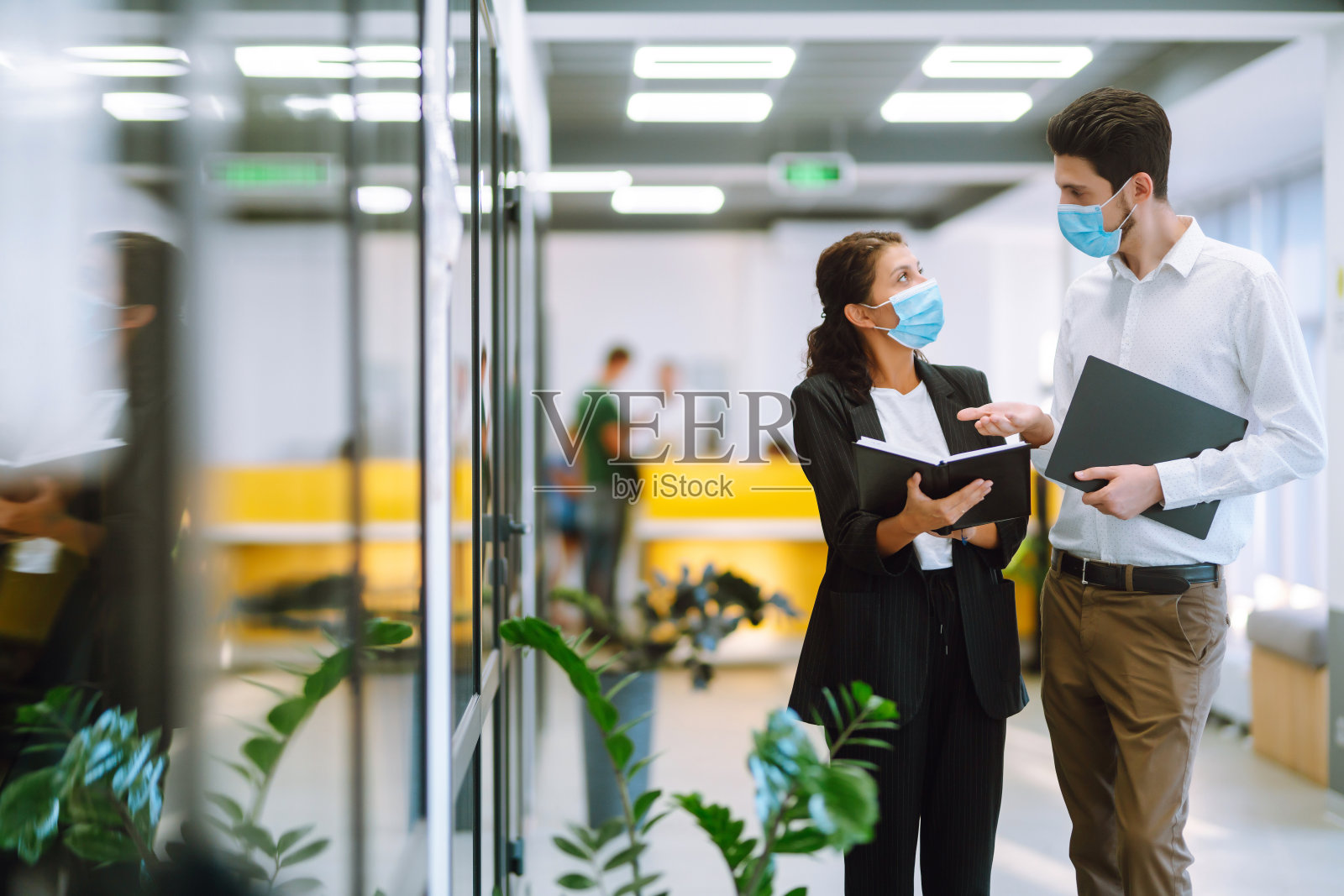 带着医用口罩的同事在办公室一起讨论工作问题。照片摄影图片