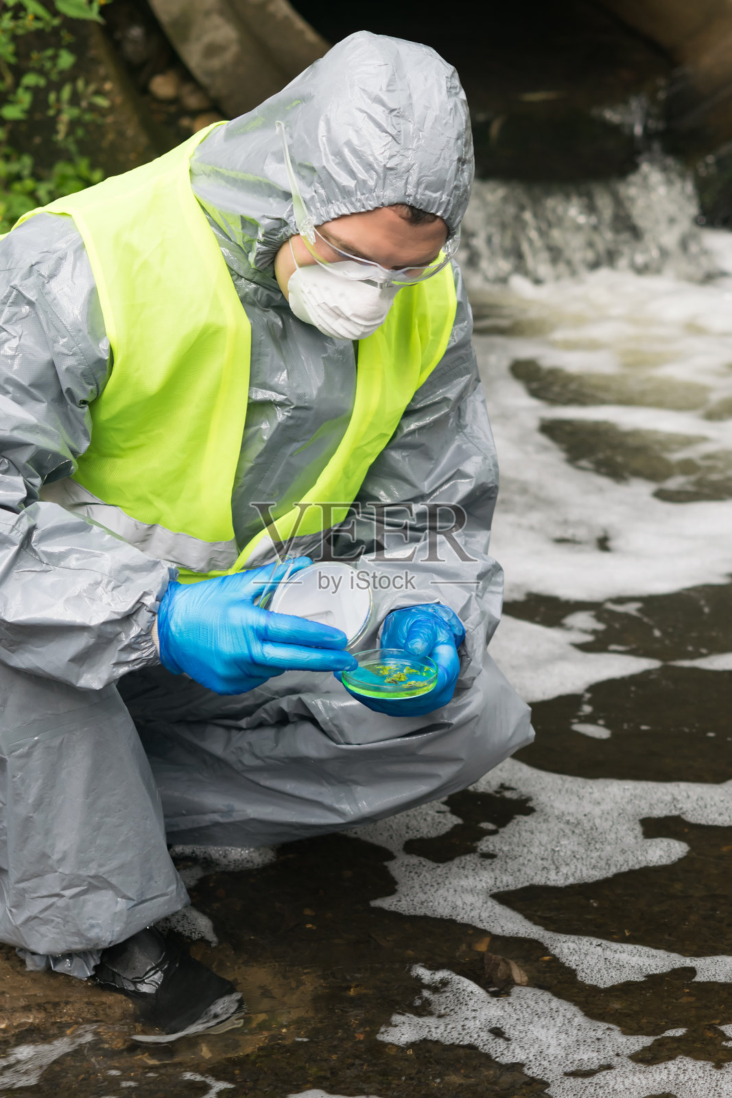 一名穿着防护服的男子拿着一个装有植物样本的培养皿，在加入试剂后观察培养皿中的反应照片摄影图片