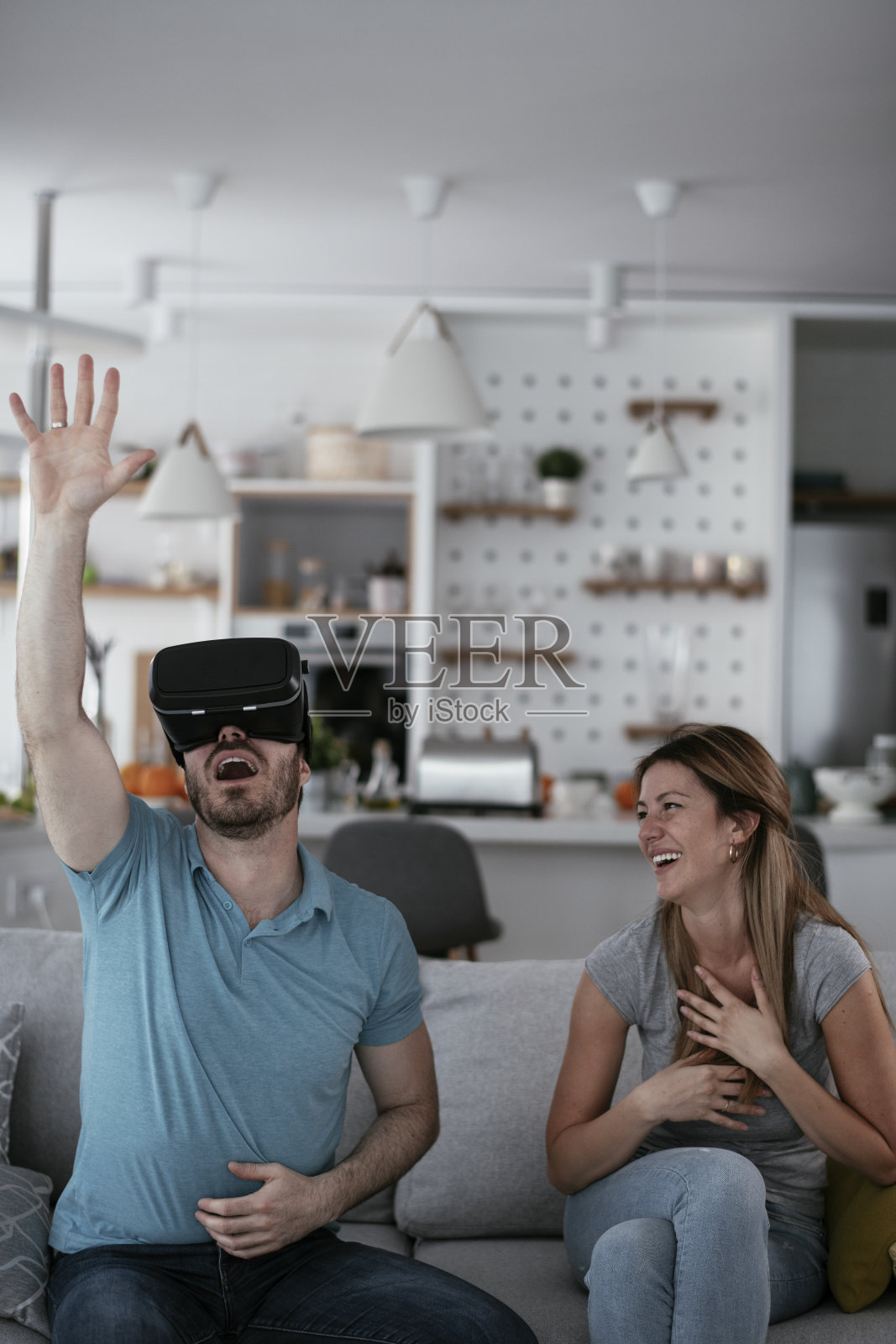 微笑的年轻人使用VR头盔在家沙发上。照片摄影图片