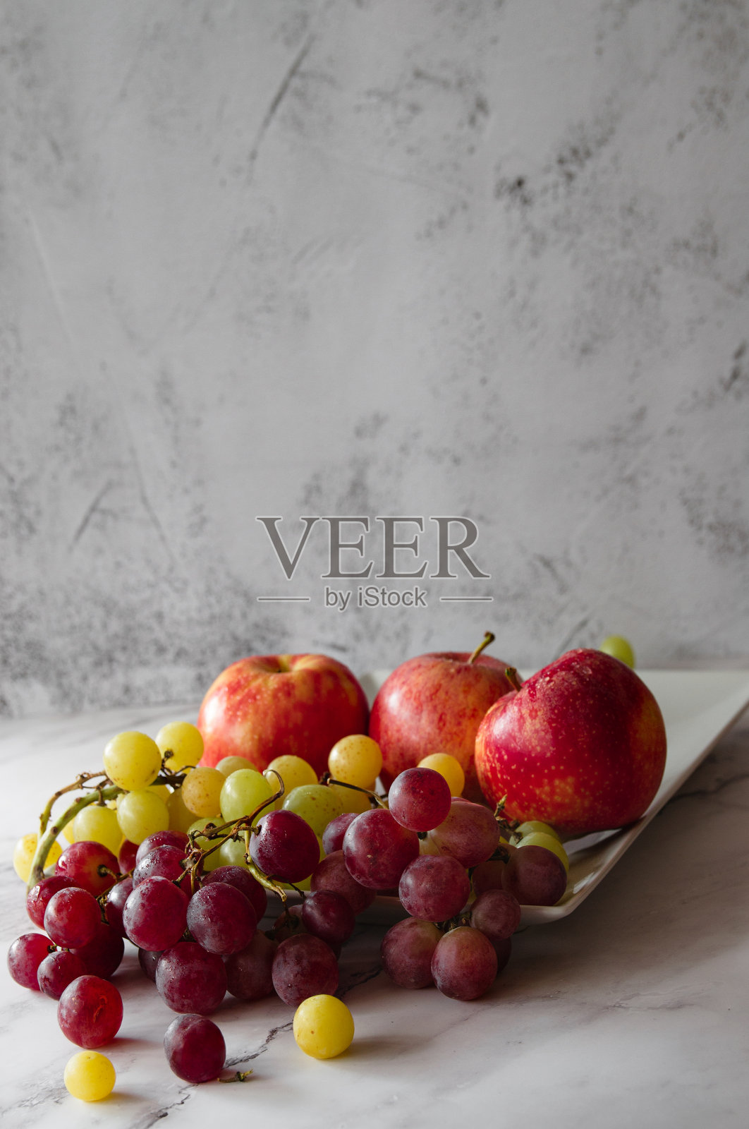 白色大理石桌子上有几个红苹果和紫色和黄色的葡萄。典型的秋天水果照片摄影图片