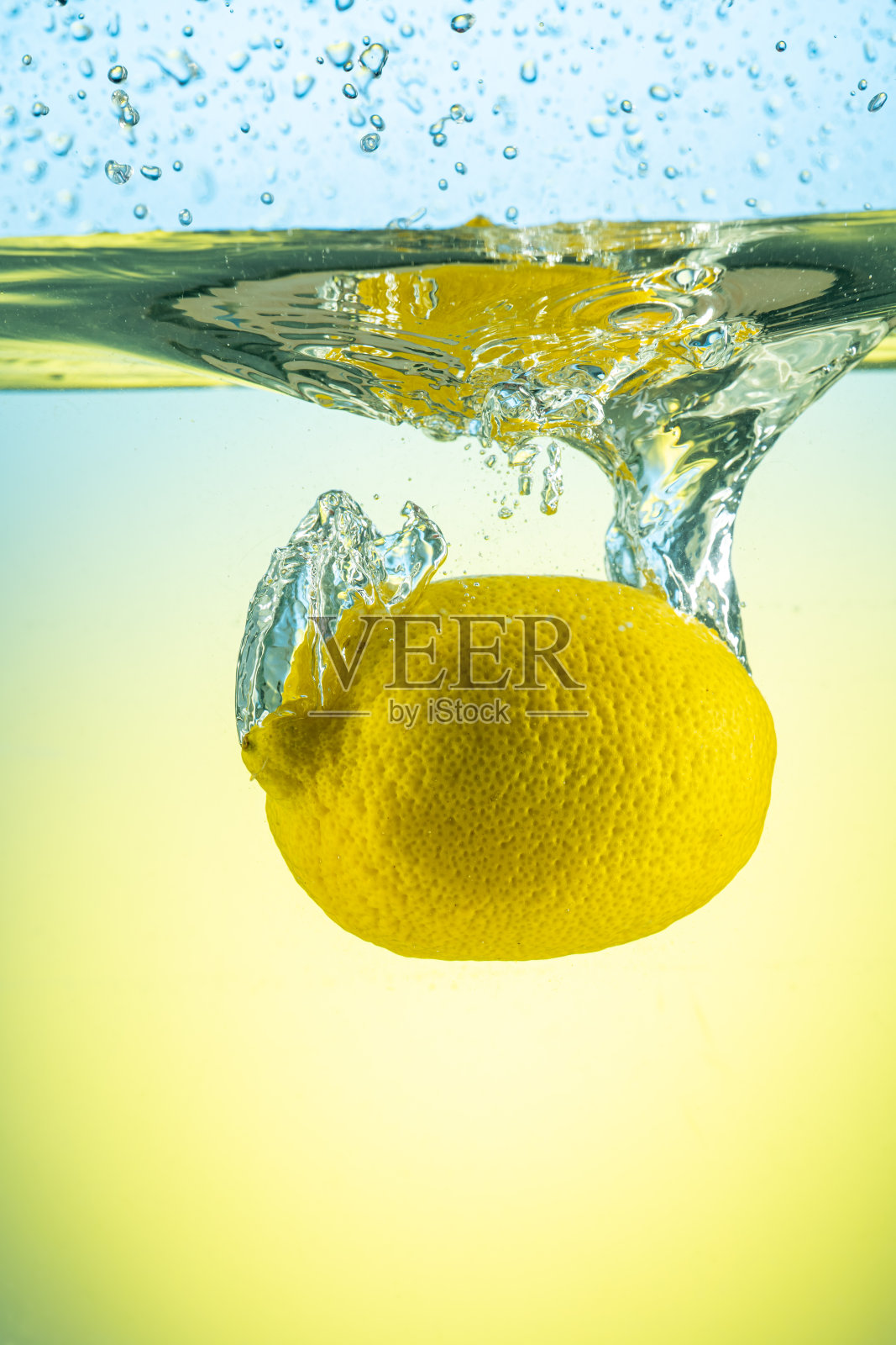 整个黄色柠檬落在水中，溅在渐变背景上照片摄影图片