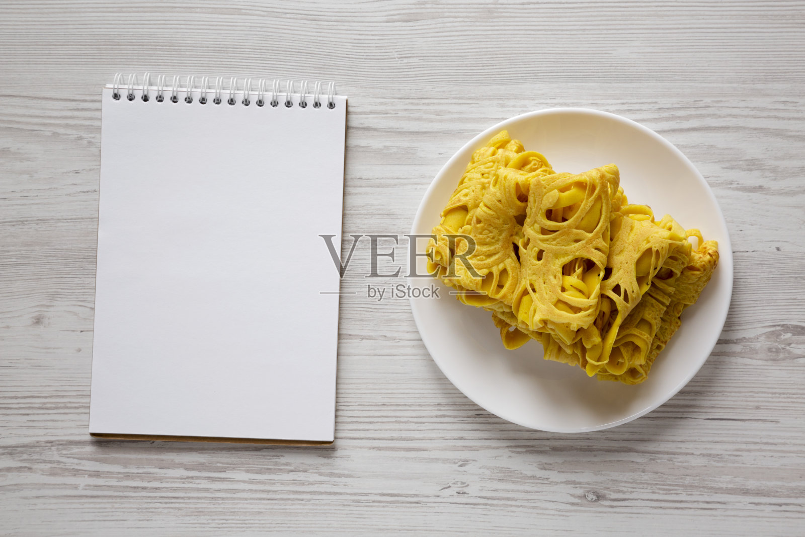 白色盘子上自制的煎饼网，白色木质背景上的空白记事本，俯视图。平躺着，从上面俯视。副本的空间。照片摄影图片