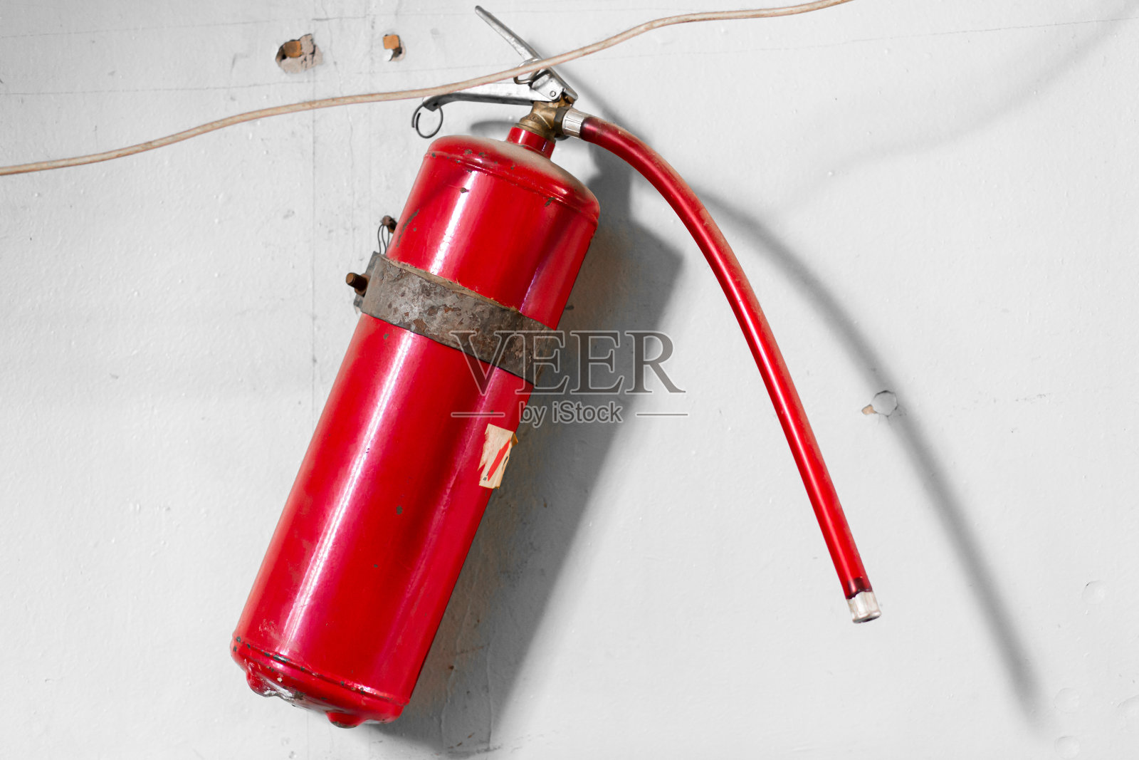 白色的墙上挂着一个红色的气球灭火器。大楼防火安全照片摄影图片
