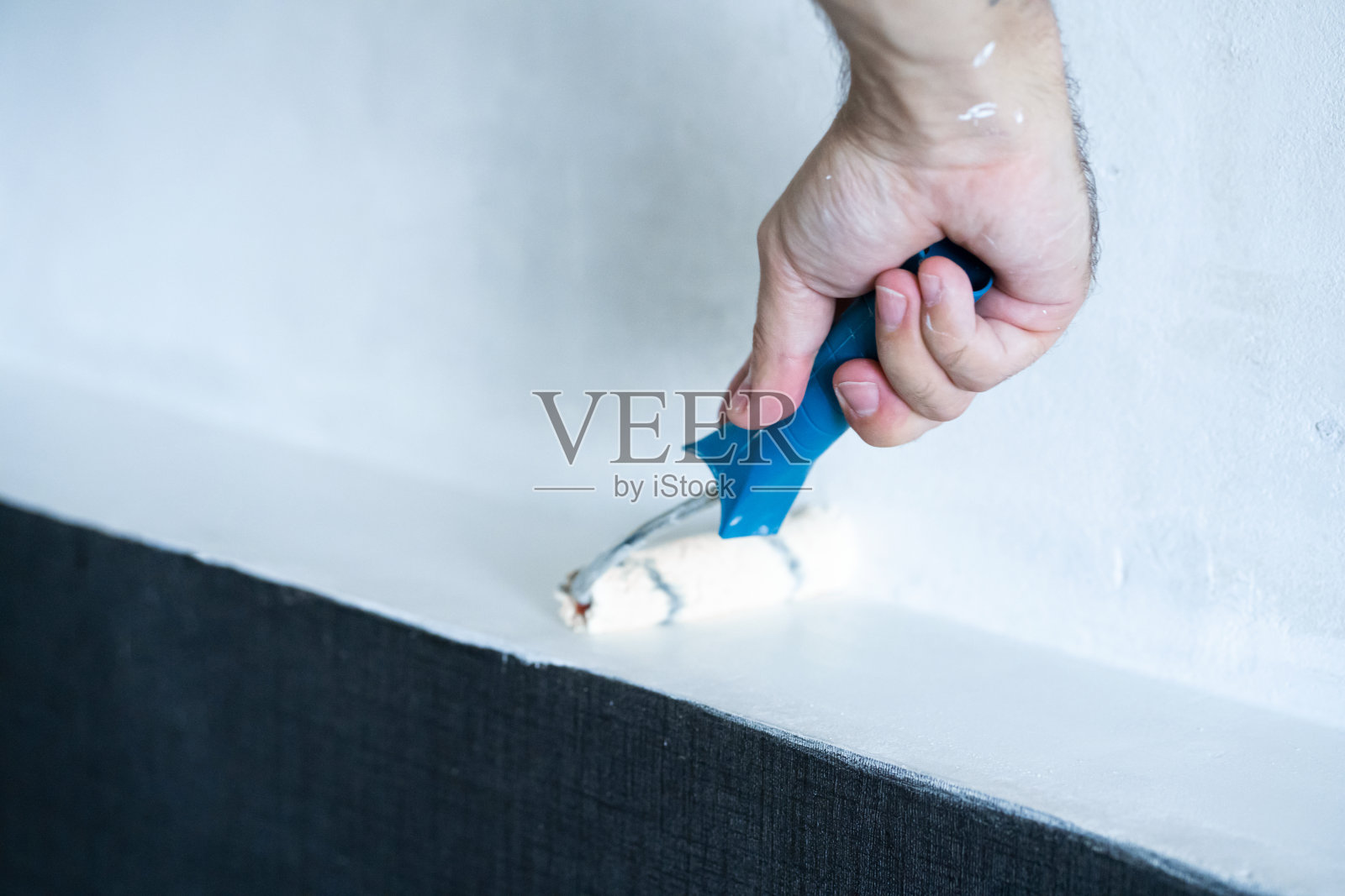 房屋装修。用白漆滚筒刷白墙。用手滚轴滚动油漆。更新墙上的油漆照片摄影图片