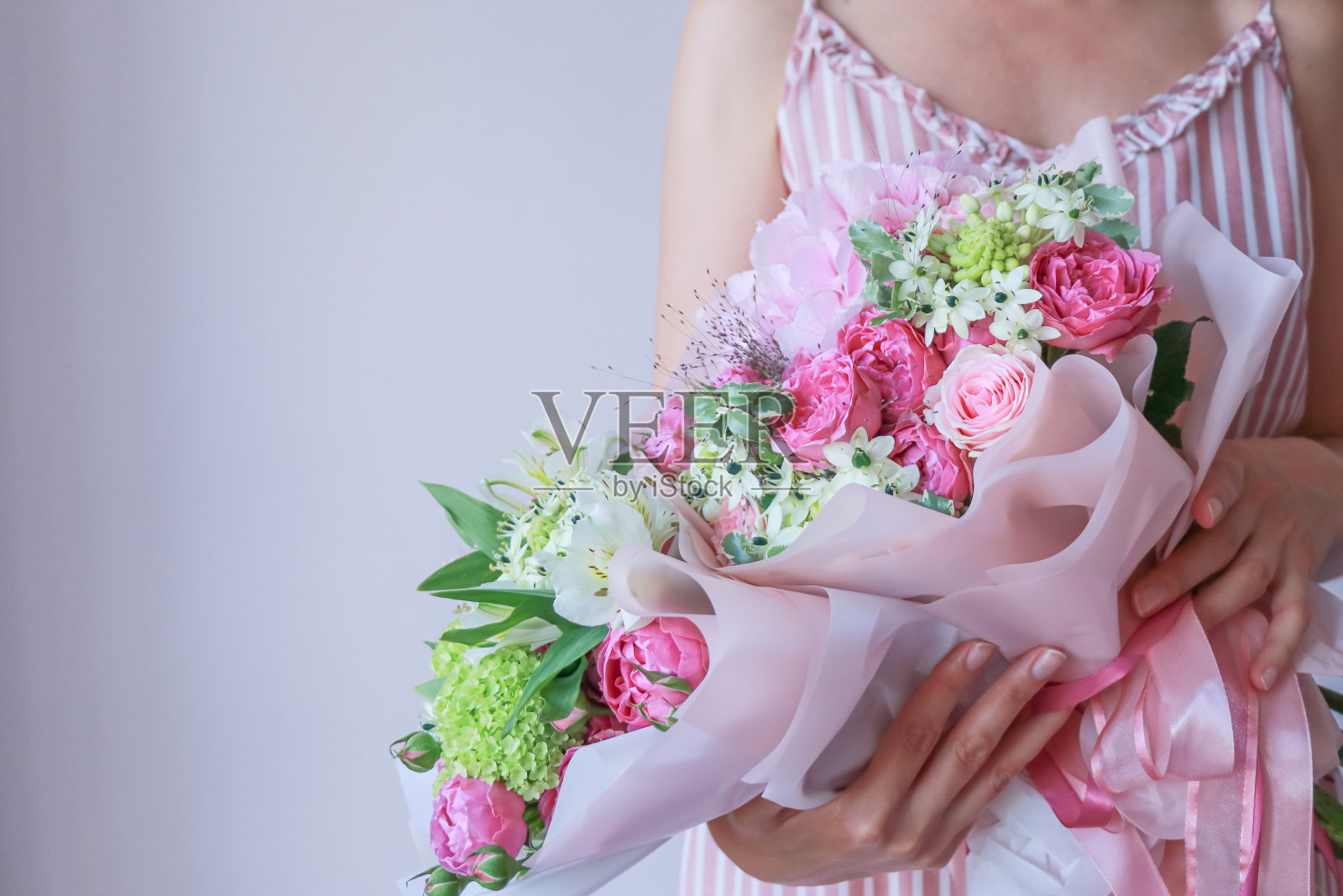 穿着粉红色背心裙的女孩手里拿着一束粉红色的绿色花束照片摄影图片