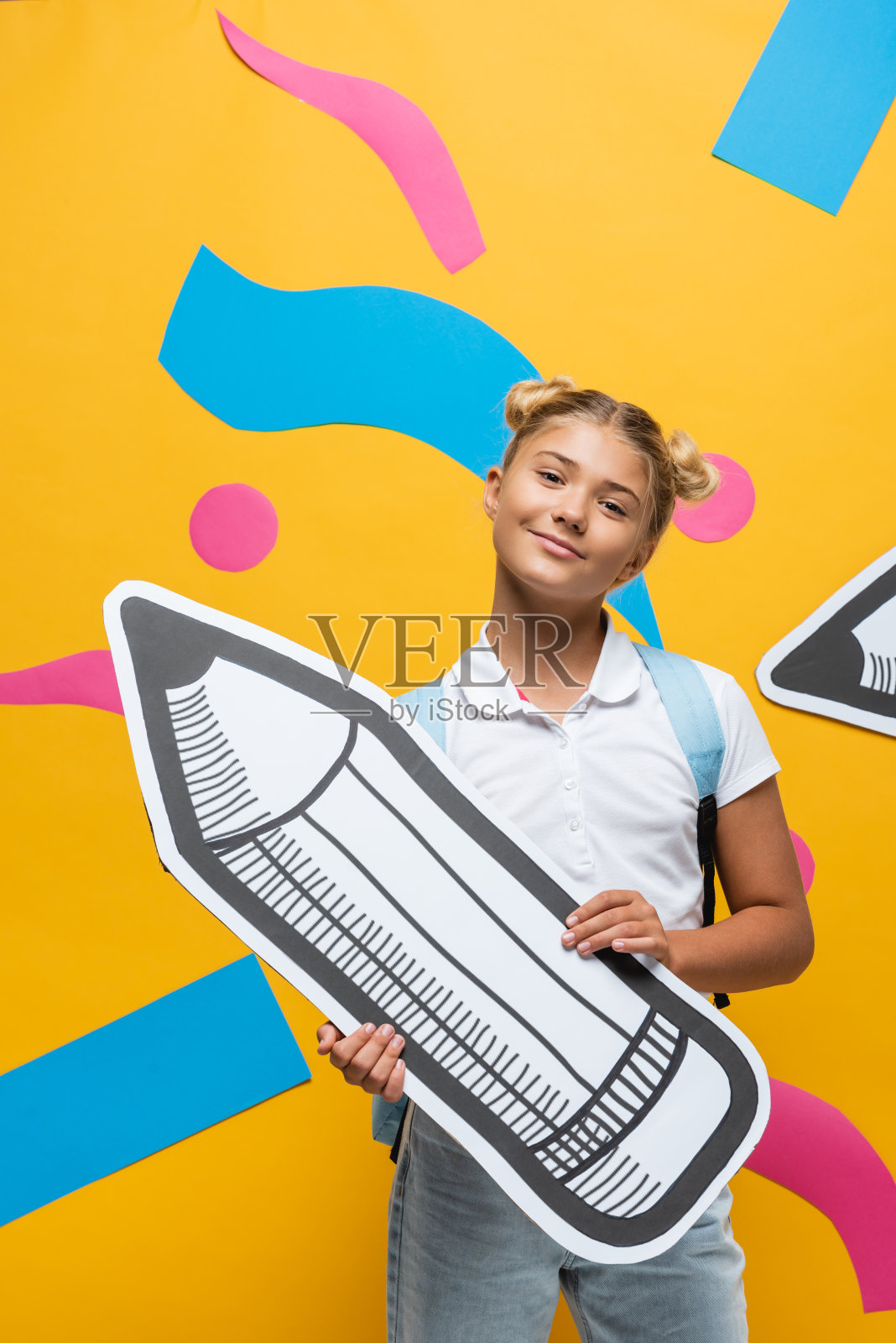 小学生拿着黄色背景的纸笔看着相机照片摄影图片