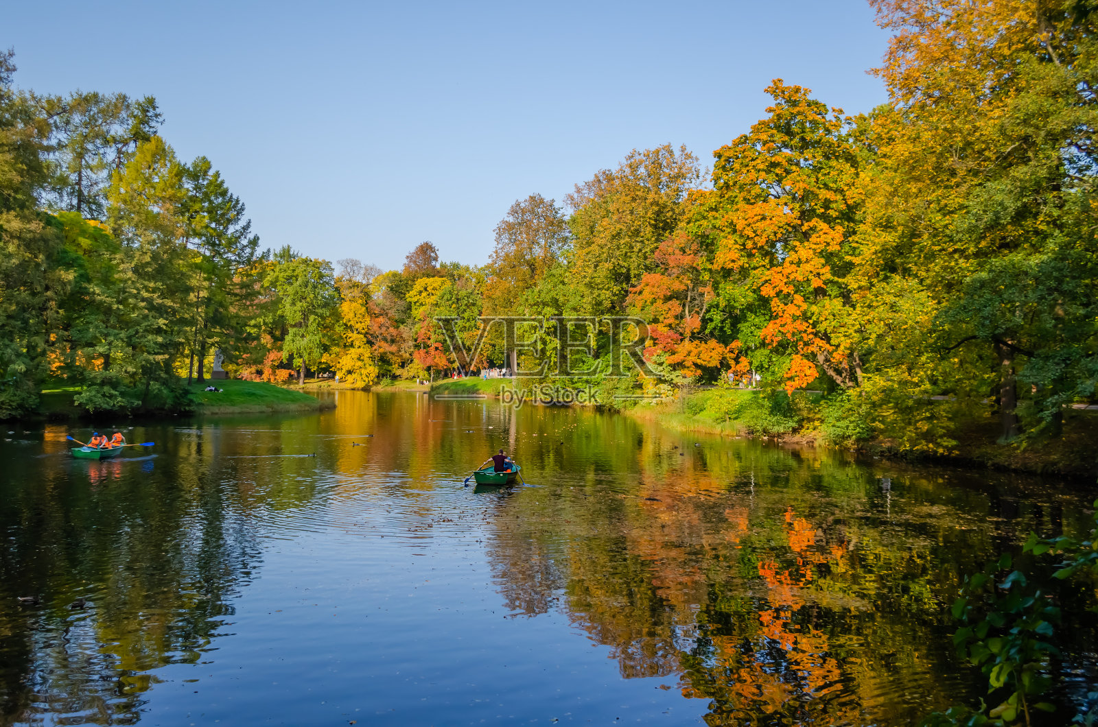 秋天的森林倒映在湖面上。游船游览公园内的湖上。照片摄影图片