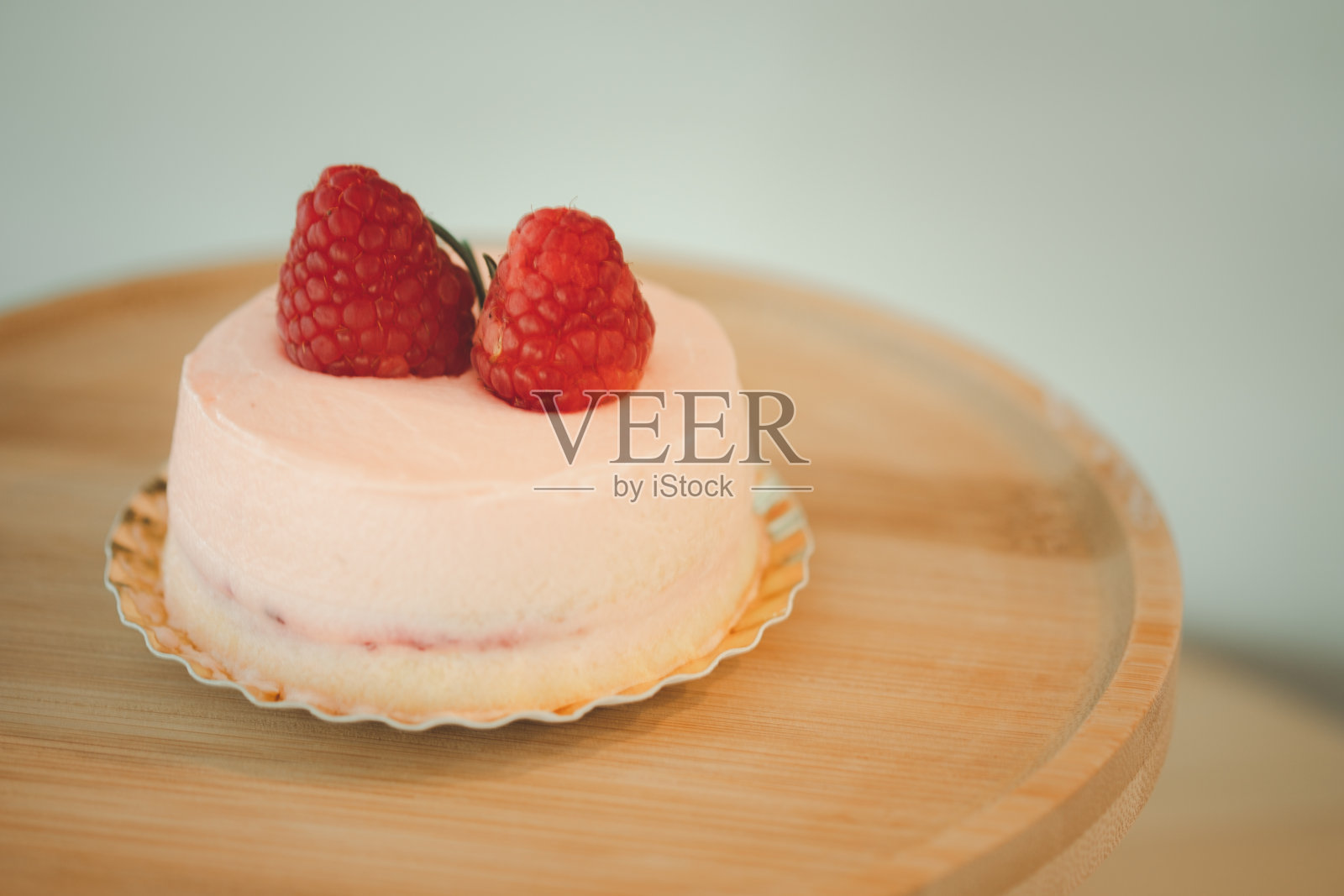 粉红色的慕斯蛋糕，上面覆盖着粉红色的奶油和浆果，放在一个圆形的木架上照片摄影图片