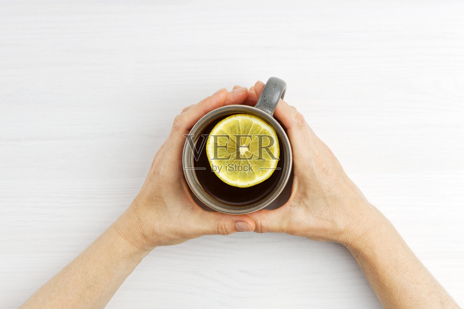 女人的手里拿着一杯热腾腾的柠檬茶。俯视图照片摄影图片