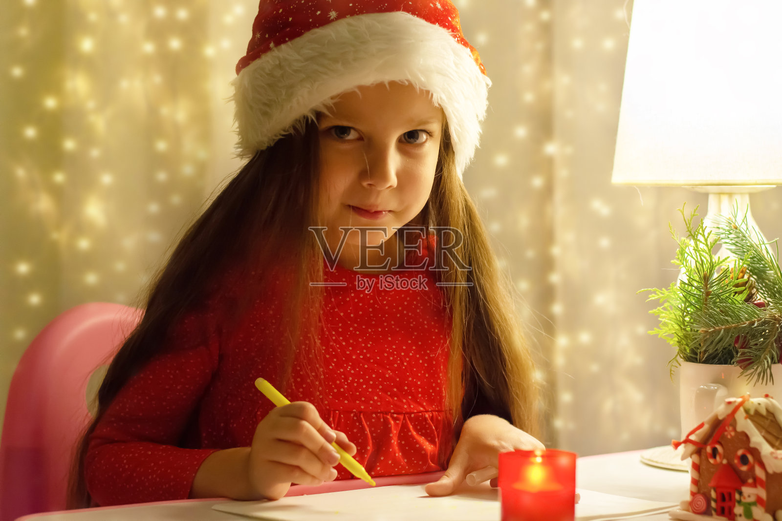 一个戴着红色圣诞帽的小女孩在给圣诞老人写信。以圣诞花环为背景。照片摄影图片