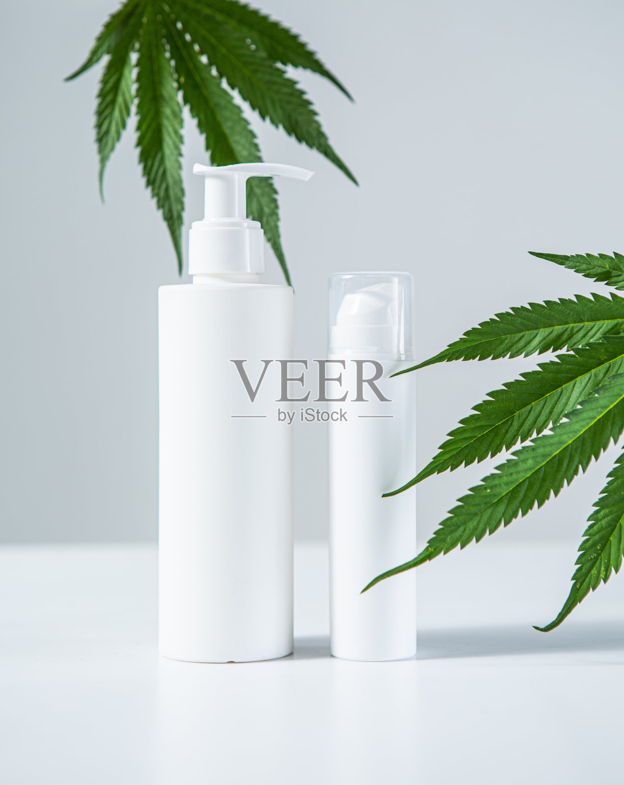 白色空白化妆瓶和麻叶在灰色工作室背景，模拟。生物有机产品，护肤理念照片摄影图片