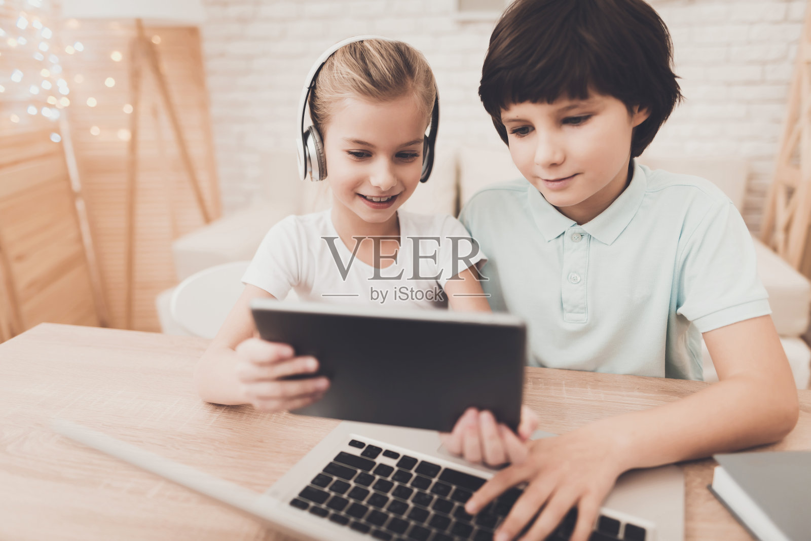 弟弟和妹妹正在使用平板电脑和笔记本电脑。照片摄影图片