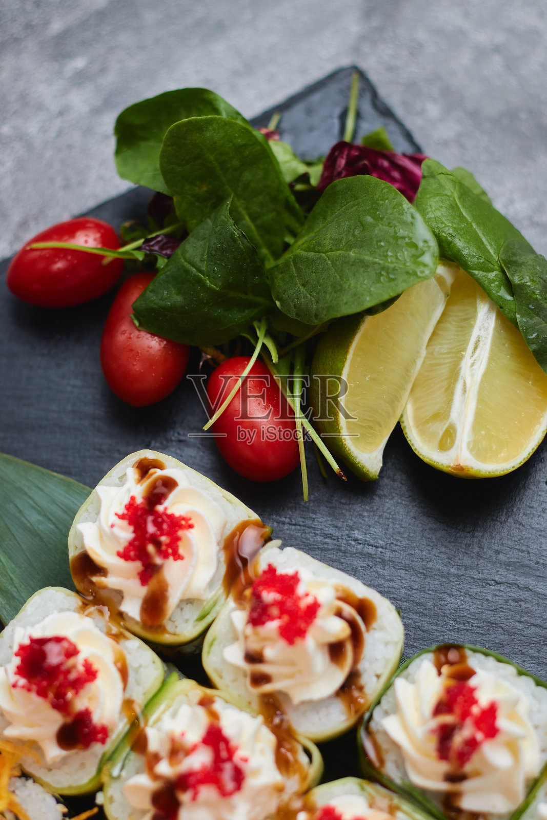 一套寿司卷放在竹叶上，配上酸橙、香草和红番茄，放在一块黑色的石板上。暗的背景照片摄影图片