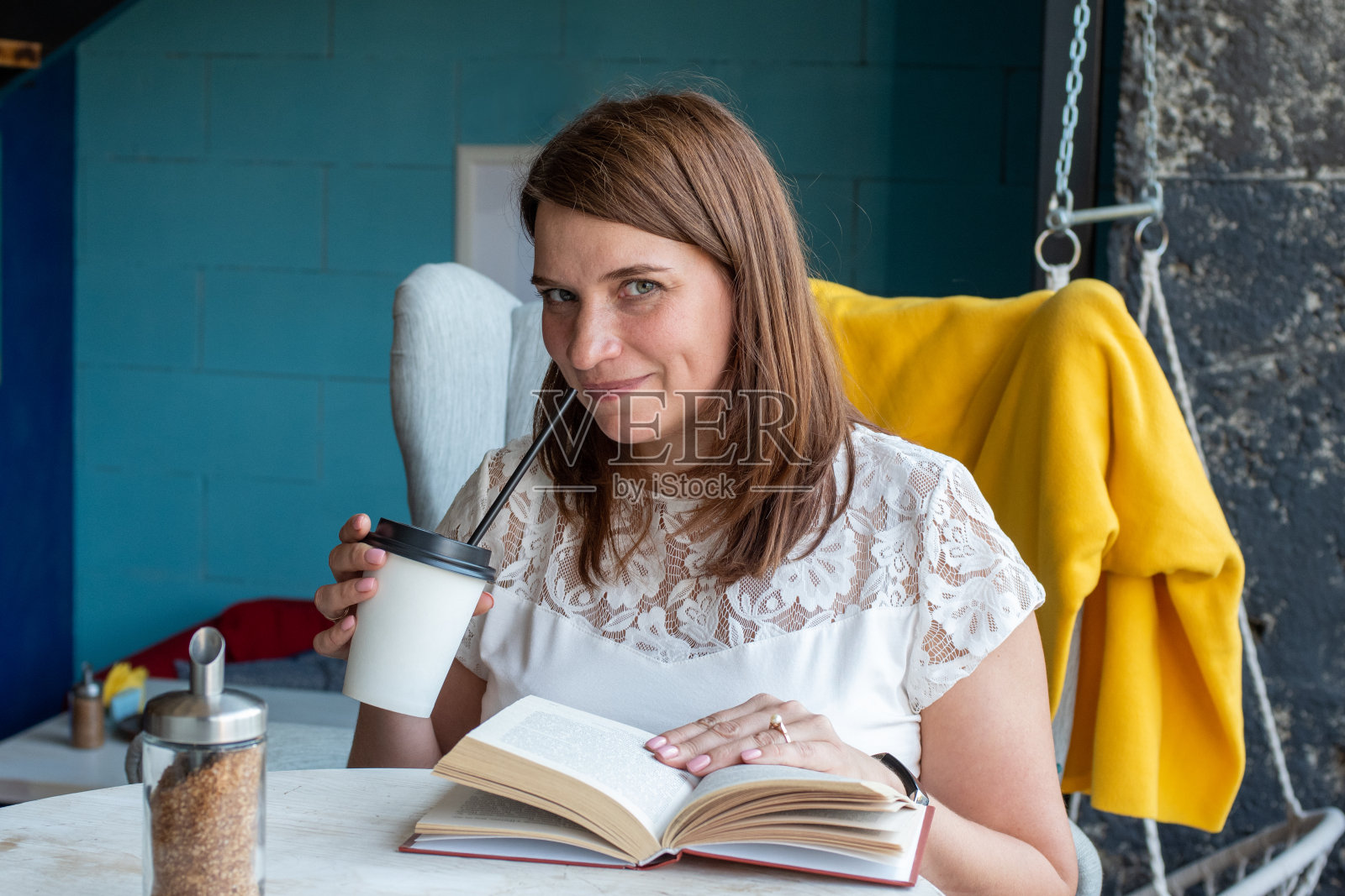一位穿着白色衬衫、一头红色长发的美丽年轻女子坐在咖啡馆的椅子上，喝着咖啡，读着书照片摄影图片