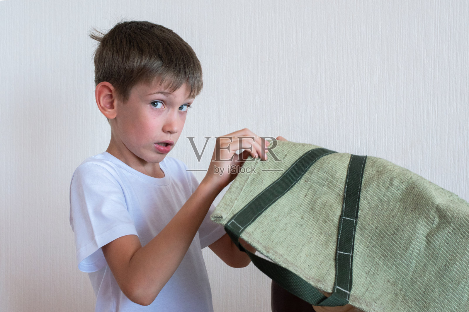 一个好奇的男孩在看一个藏在绿布后面的东西。儿童好奇心的概念照片摄影图片