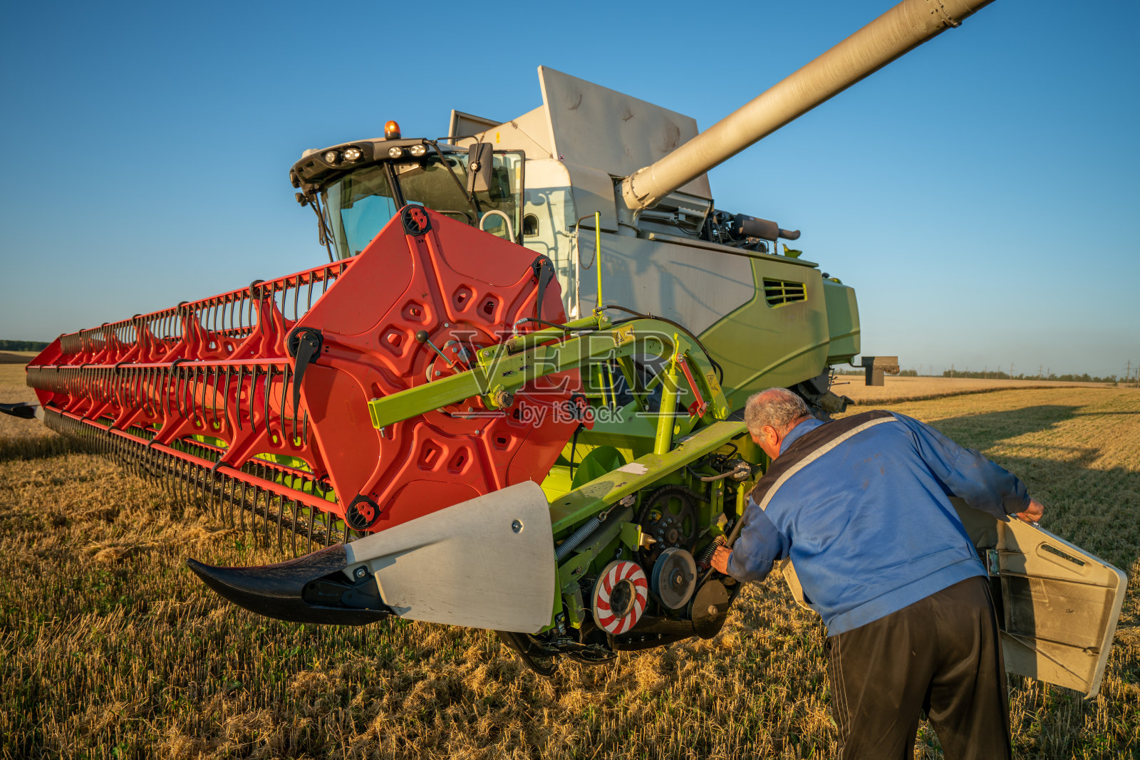 田间的机器操作员检查联合收割机的机械装置照片摄影图片