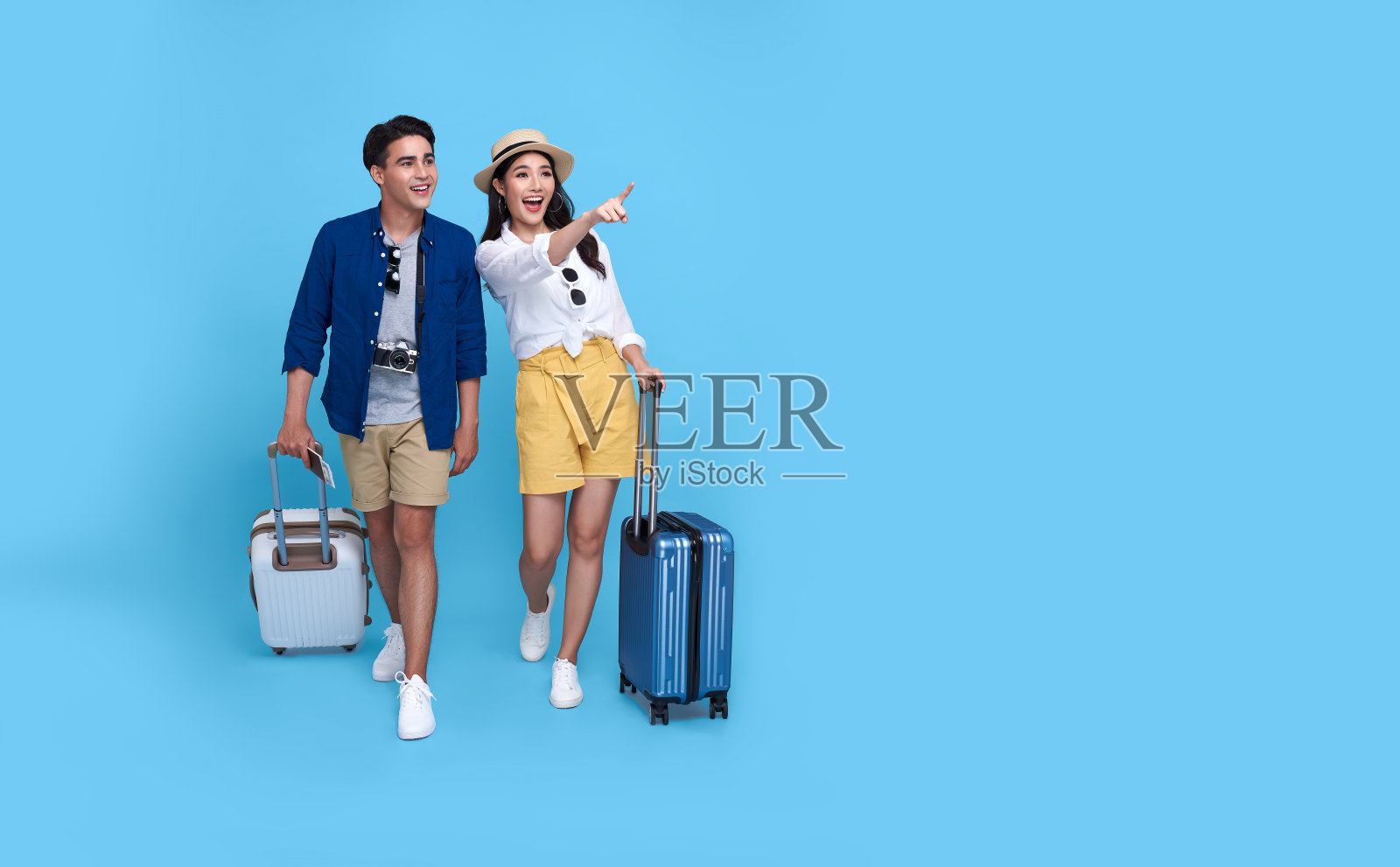 幸福的亚洲夫妇旅游手指向拷贝空间与行李将旅行在孤立的蓝色背景。照片摄影图片
