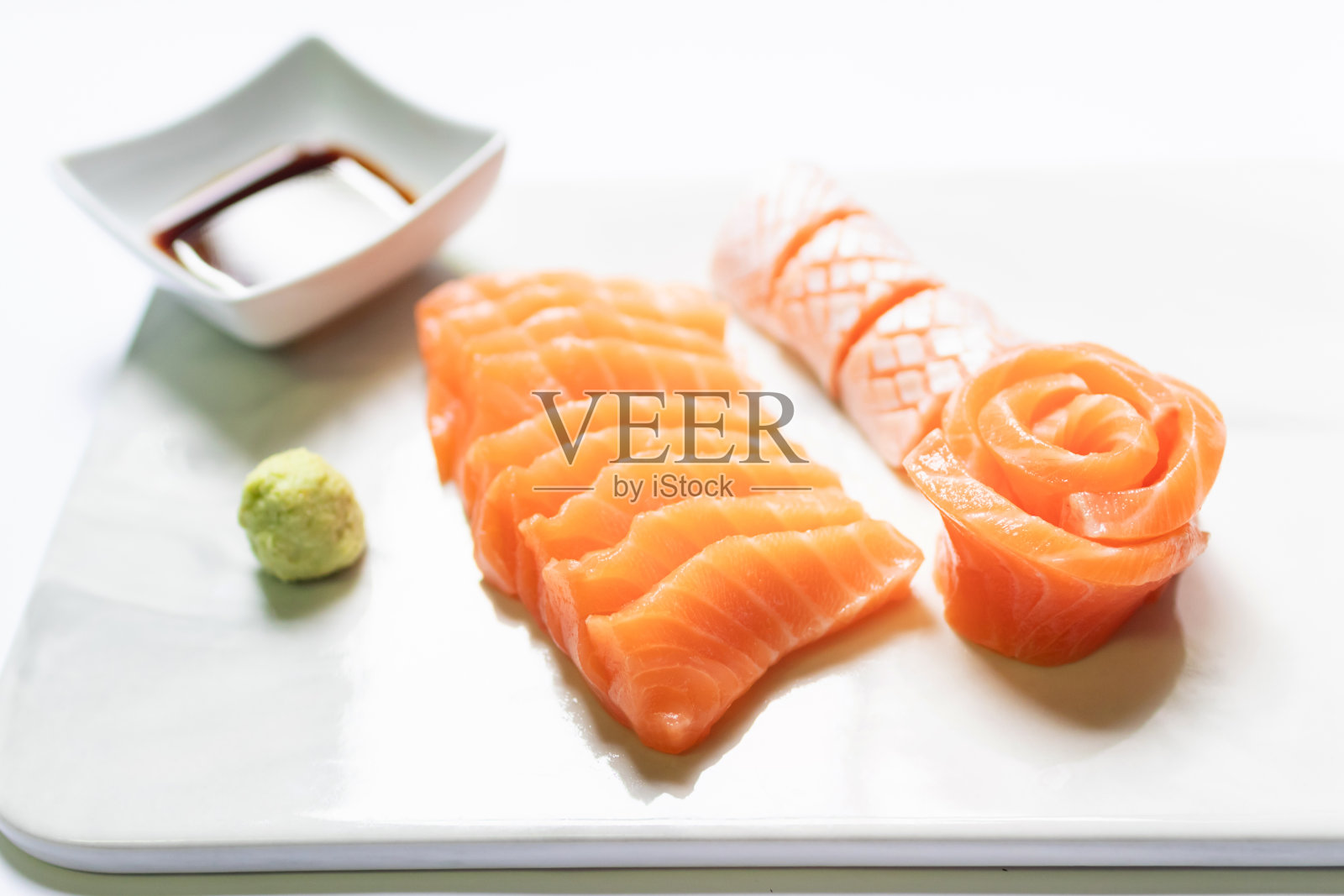 用筷子夹着大理石盘子里的新鲜鲑鱼、牛头鱼生鱼片和芥末。照片摄影图片