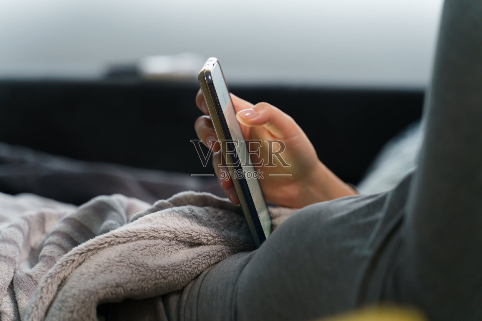 近距离看手机在不知名的白人妇女躺在家里的床上-休闲活动上网浏览或花时间在社交媒体上-反社会的概念专注于智能手机照片摄影图片