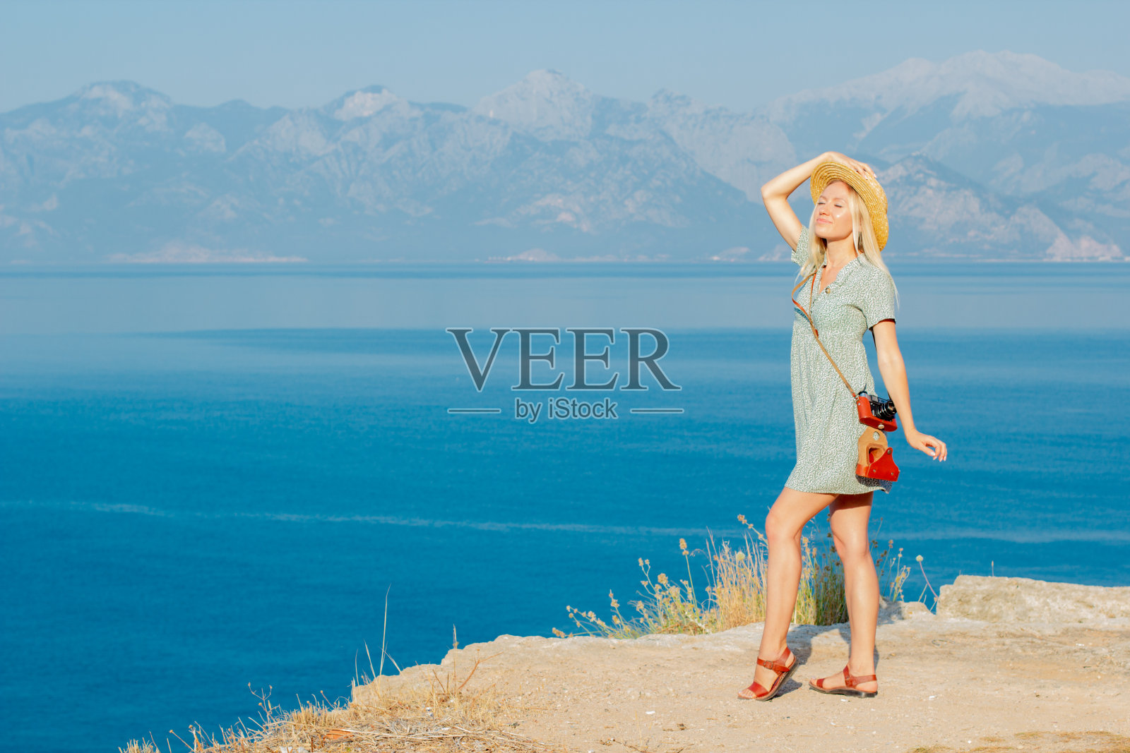 一个戴着帽子的女人在海边的悬崖边上。照片摄影图片