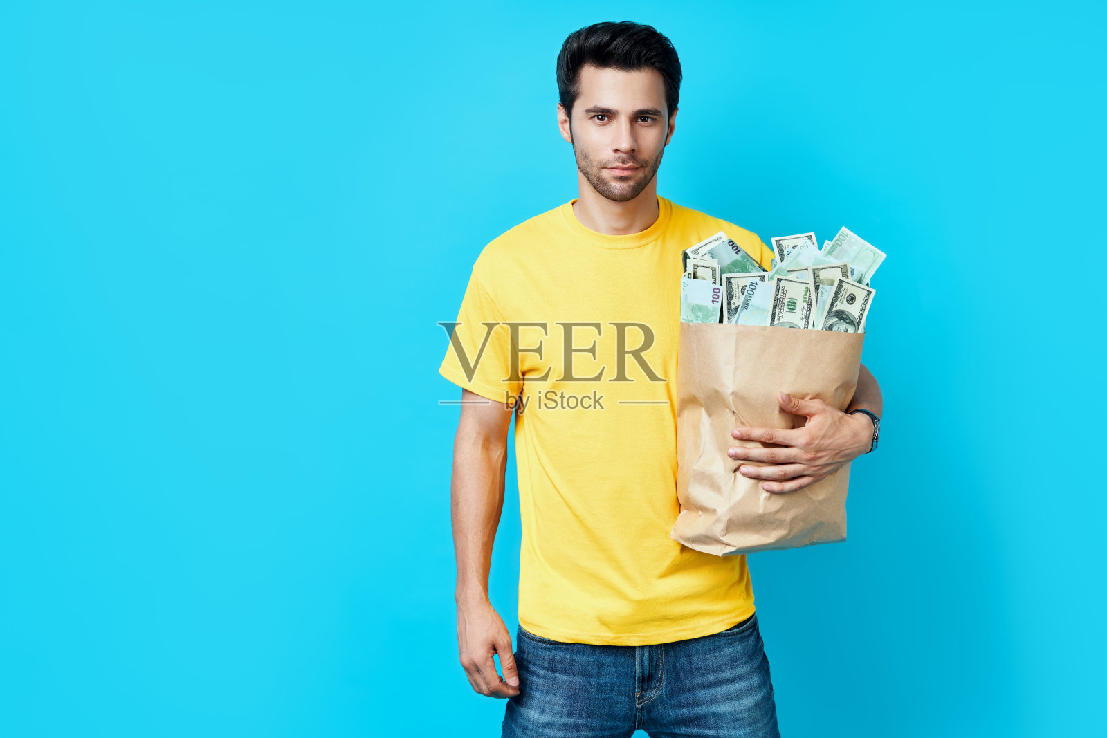 英俊的男人拿着纸袋装满了钱孤立在蓝色背景照片摄影图片