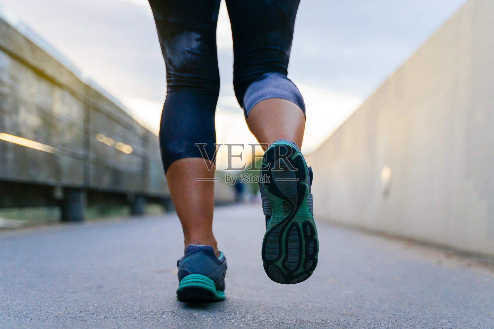 近距离拍摄年轻女子在日落时在公园里跑步，背景模糊——健康生活方式的概念照片摄影图片