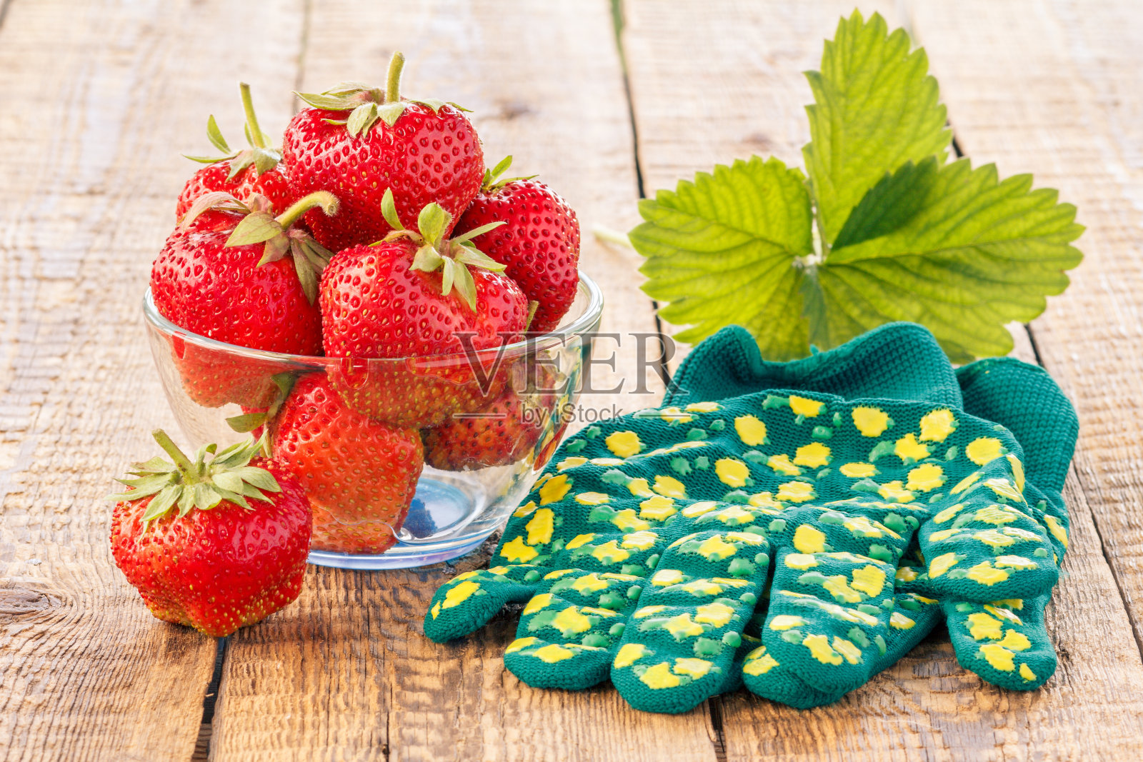 熟透的红草莓放在玻璃碗里，手套放在旧木箱上照片摄影图片