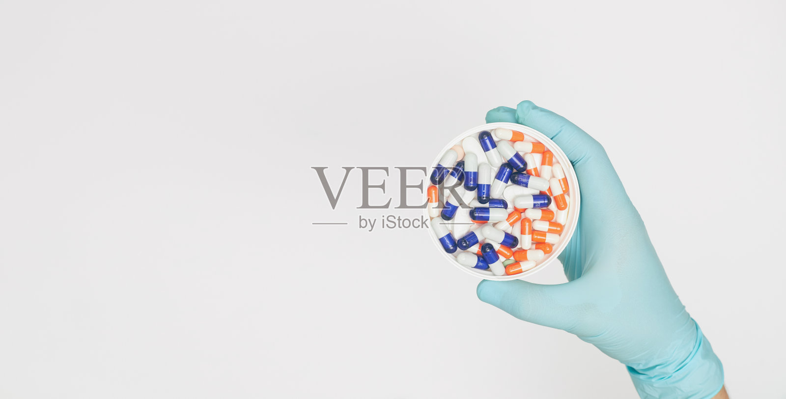 手拿一只手套放在一个装有胶囊的盒子里，放在一个白色背景的概念上，将COVID-19的预防平躺着照片摄影图片