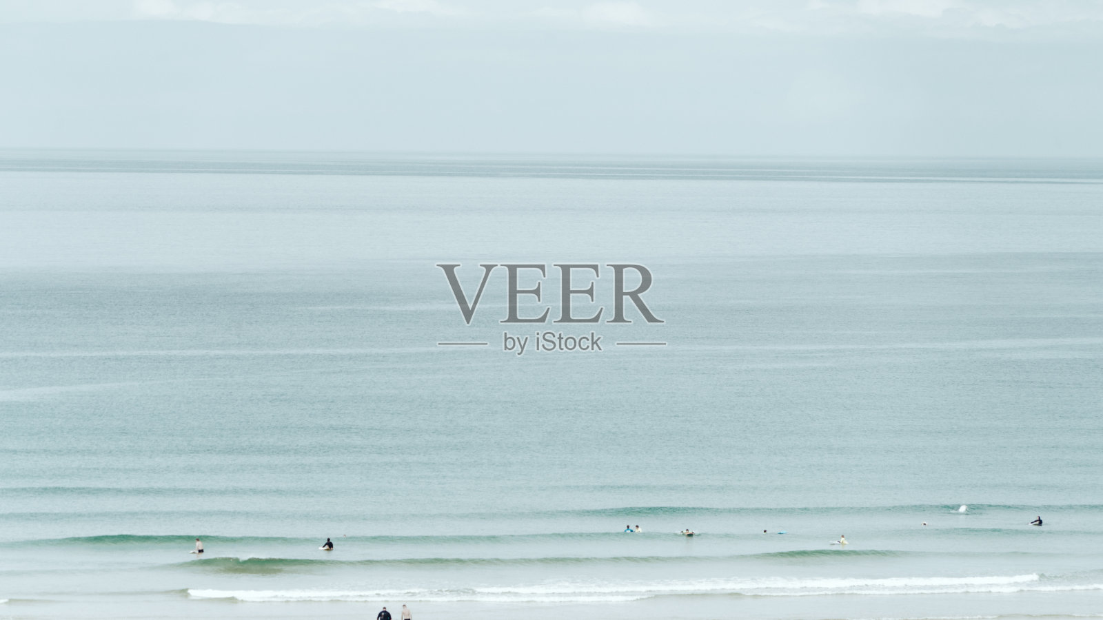 海浪涌向海岸，一些冲浪者在等着抓一个照片摄影图片