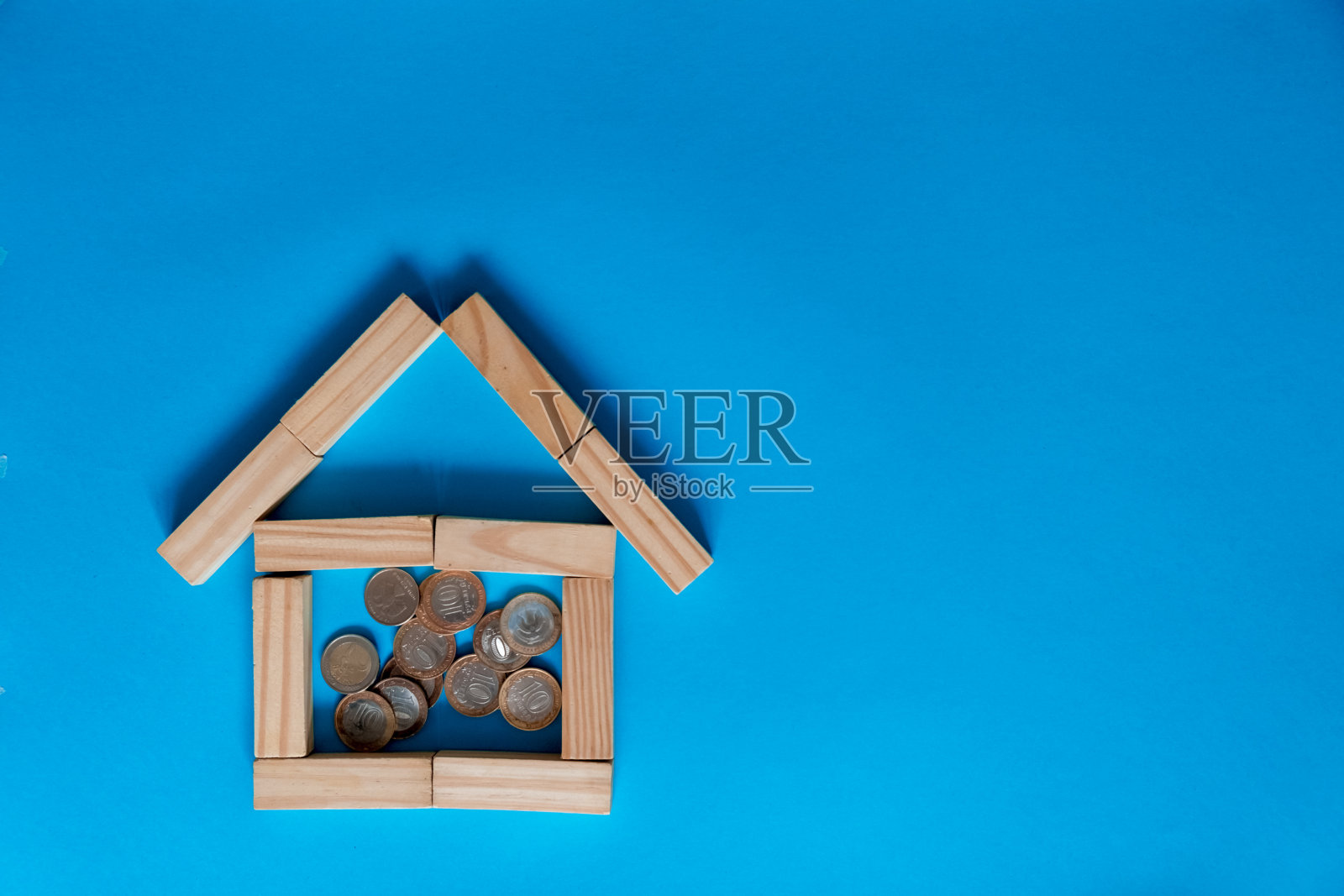 特写硬币与模型家在木桌子上的蓝色背景照片摄影图片