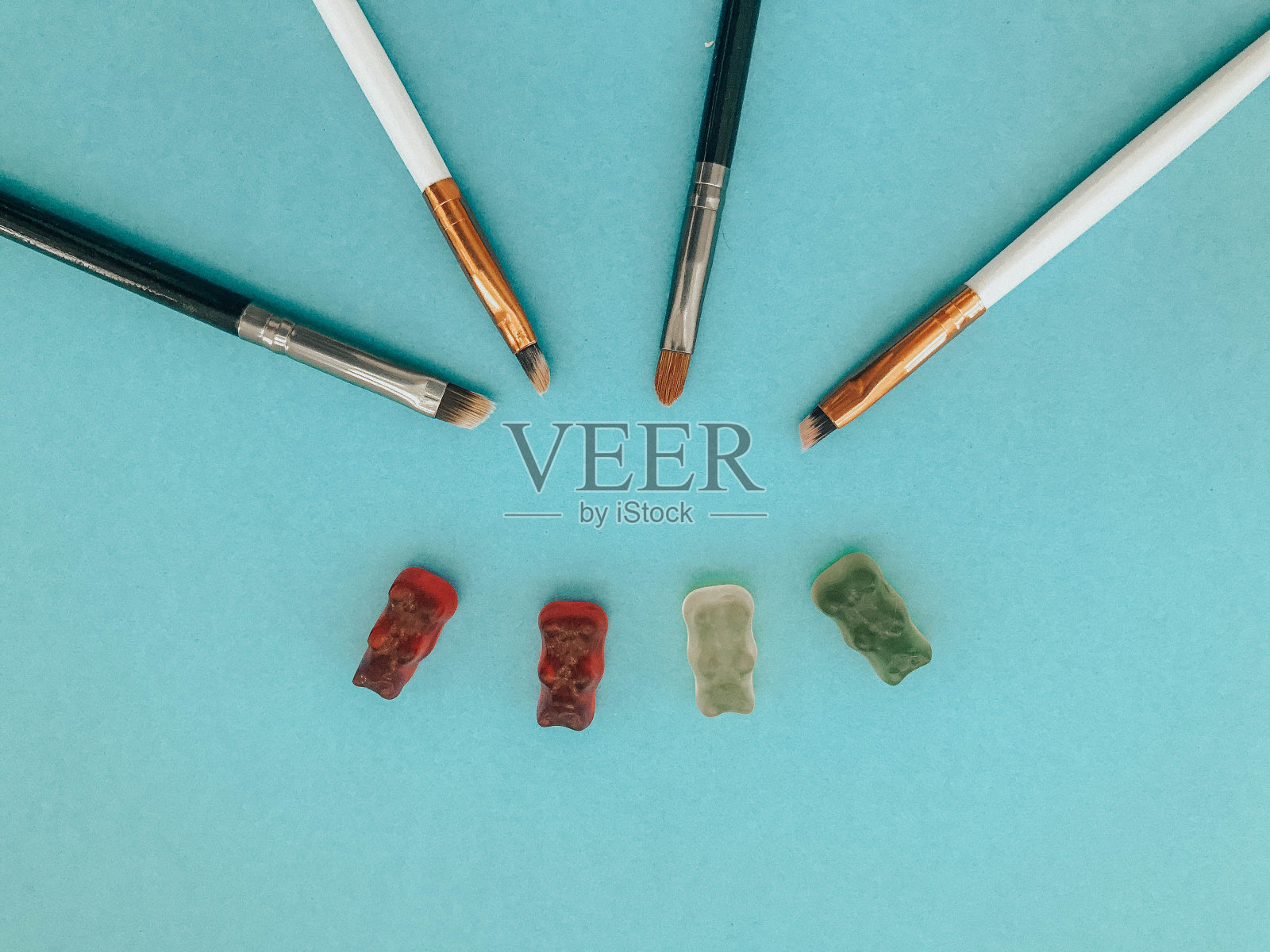 化妆刷放在蓝色哑光背景旁边的小熊软糖。橡皮糖会用化妆刷上色。小熊软糖的毛刷照片摄影图片